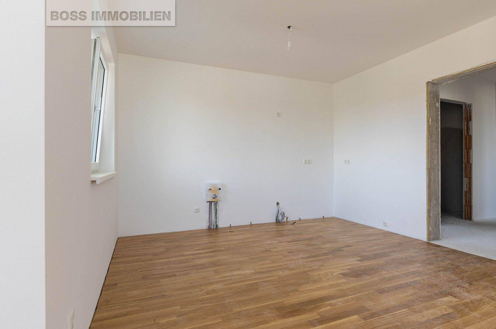 Leerer Küchenbereich mit Holzboden und Anschlüssen für eine zukünftige Einbauküche.