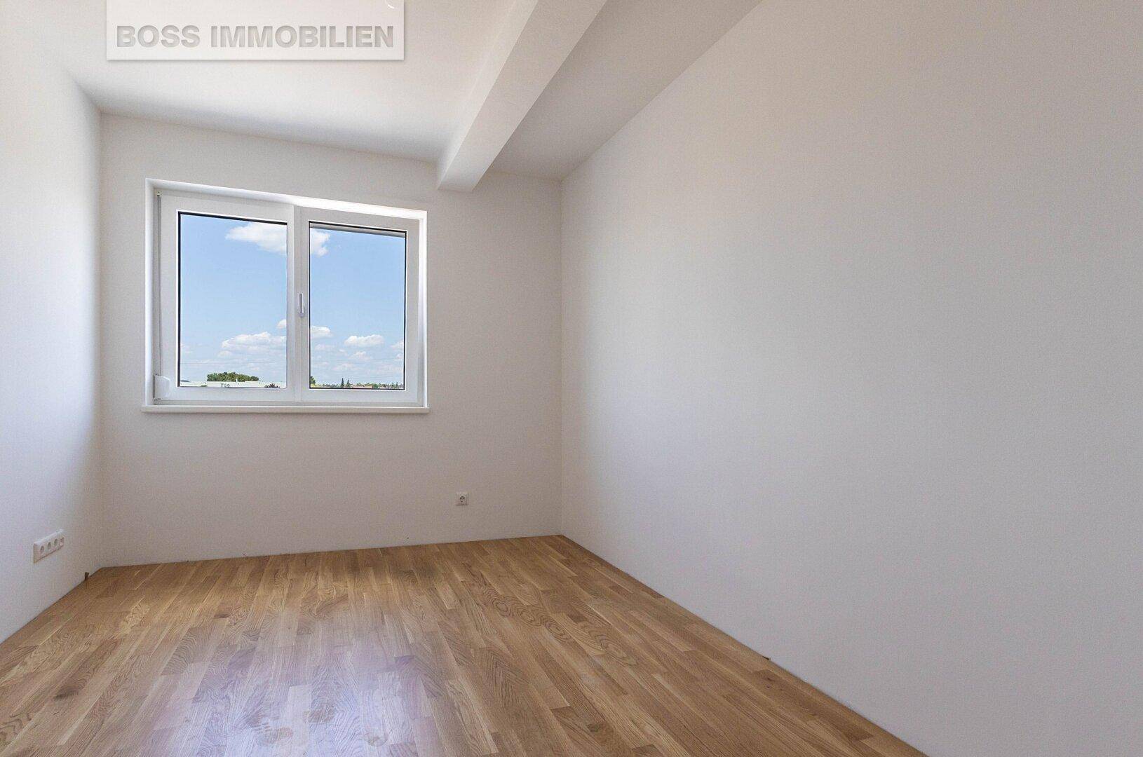 Leeres Zimmer mit Holzboden, einem Fenster und einer sichtbaren Deckenbalkenstruktur.