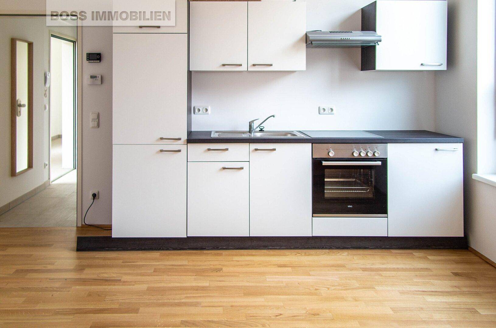 Helle Einbauküche mit weißen Schränken, dunkler Arbeitsplatte und Holzfußboden in einem modernen Apartment.