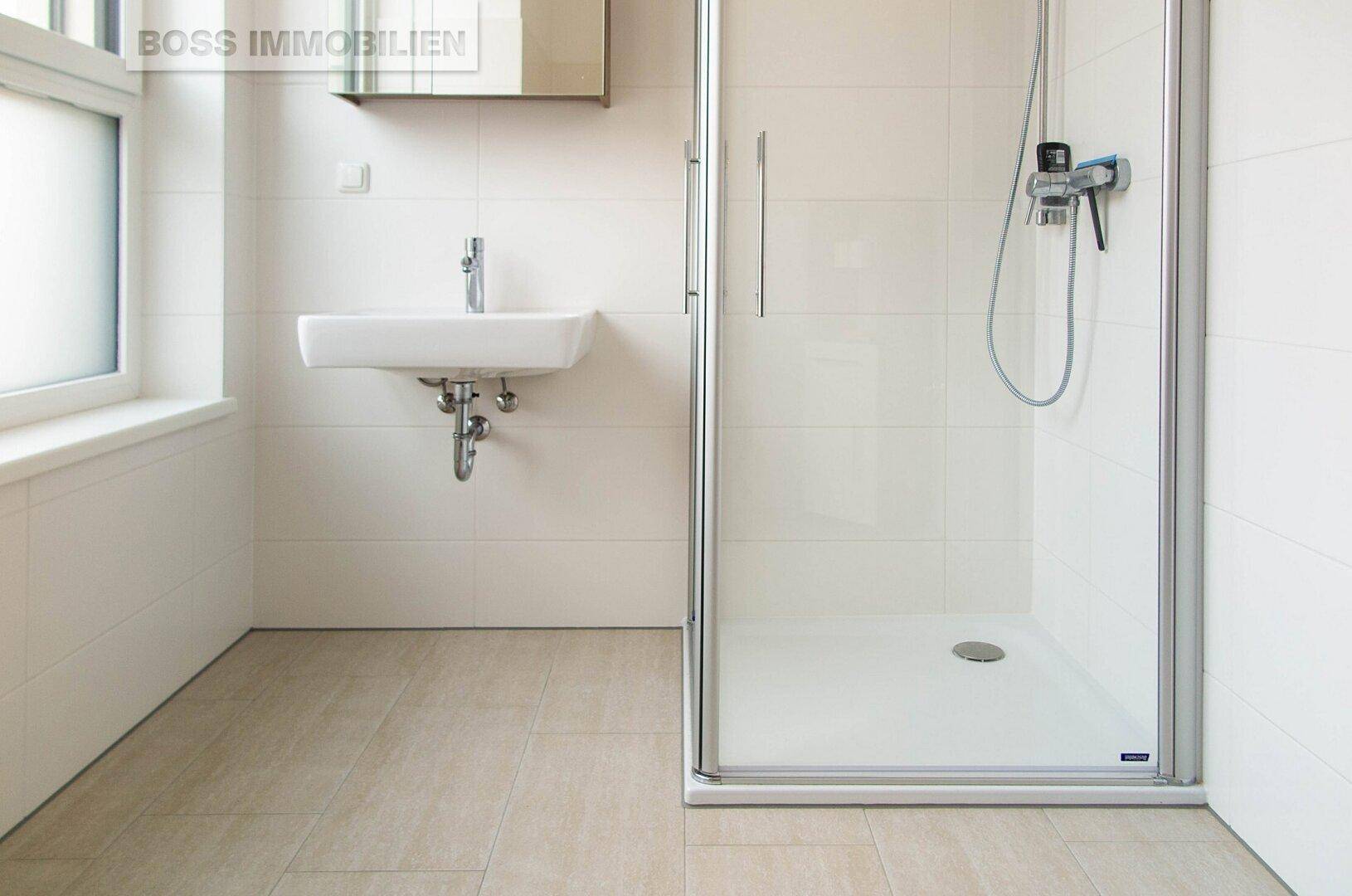 Modernes Badezimmer mit Duschkabine, Waschbecken, hellen Fliesen und einem Fenster für Tageslicht.