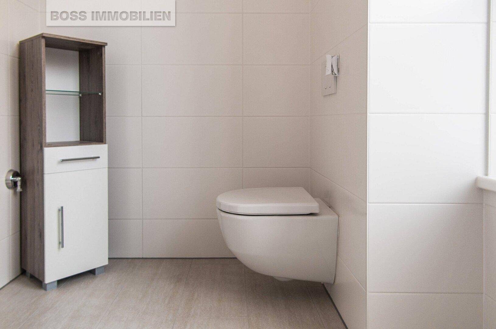 Helles Badezimmer mit wandhängender Toilette, einem schmalen Schrank und modernen Fliesen an Wänden und Boden.