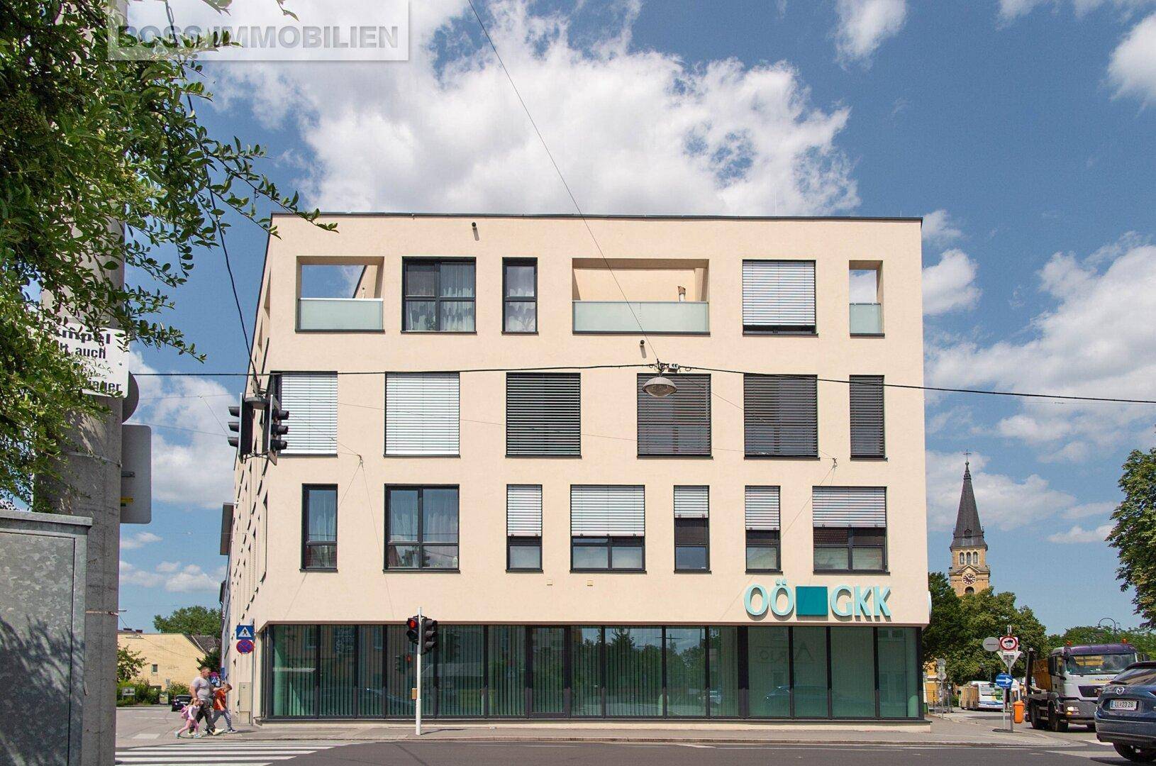 Ansicht des modernen Gebäudes mit beiger Fassade, vielen Fenstern und einem Geschäft im Erdgeschoss.