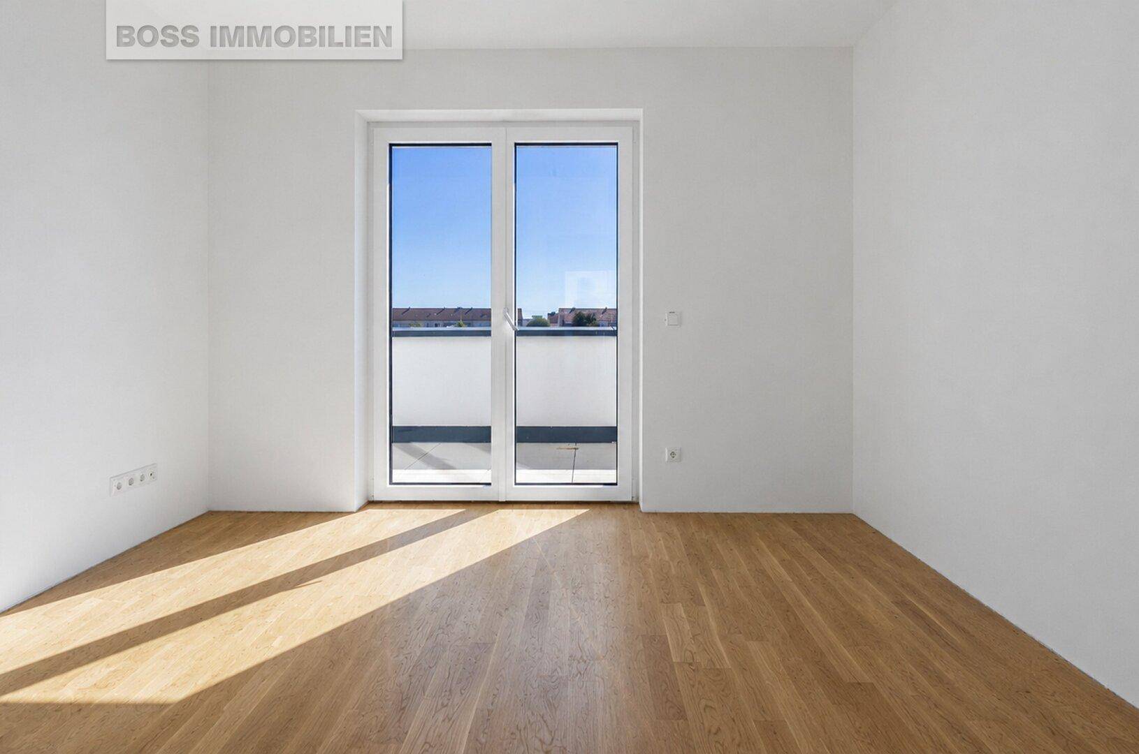 Leeres, helles Zimmer mit Parkettboden und Zugang zu einem Balkon.