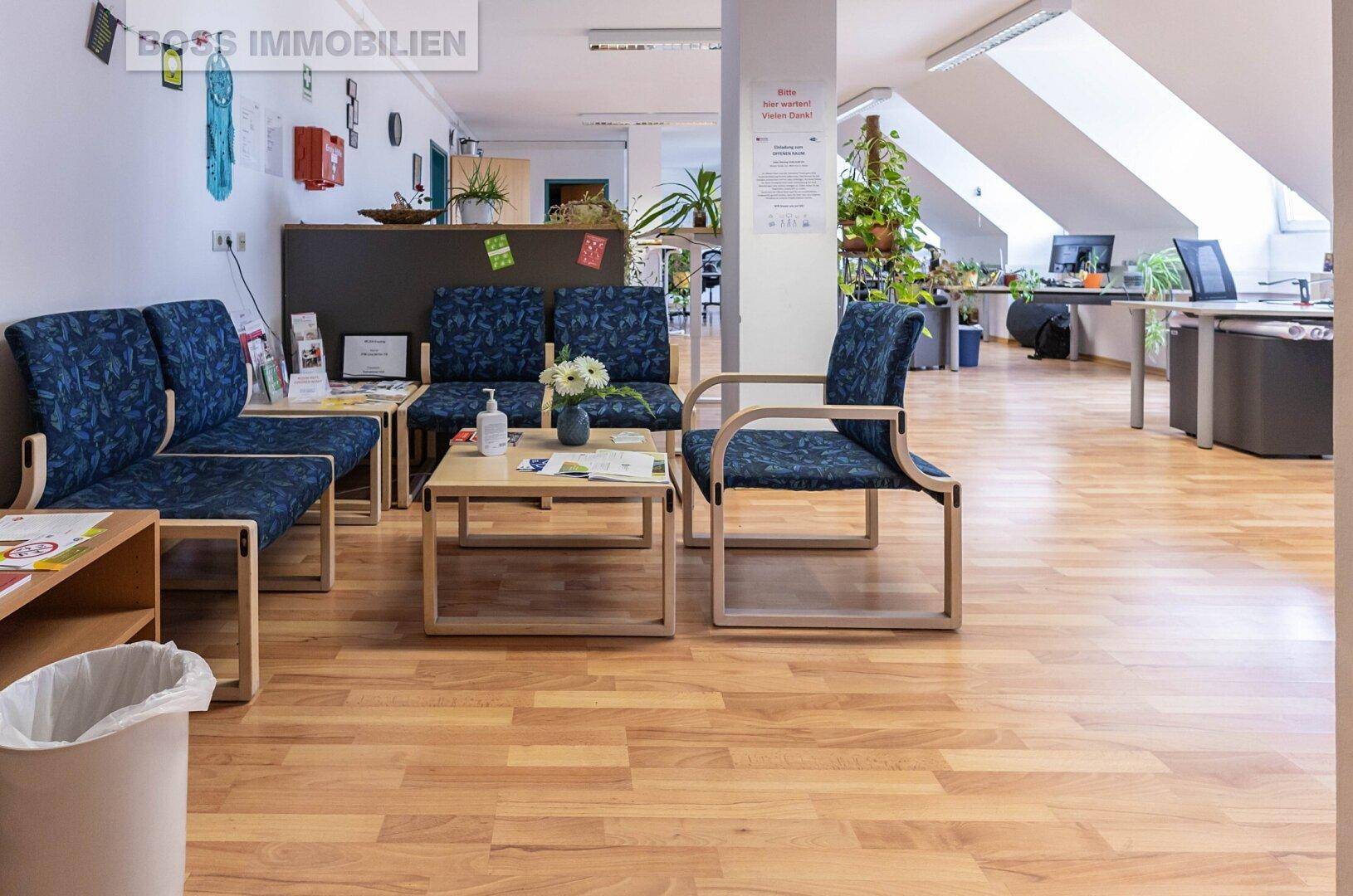 Gemütlicher Wartebereich mit blauen Sitzgelegenheiten und einem Couchtisch, angrenzend an ein offenes Büro.