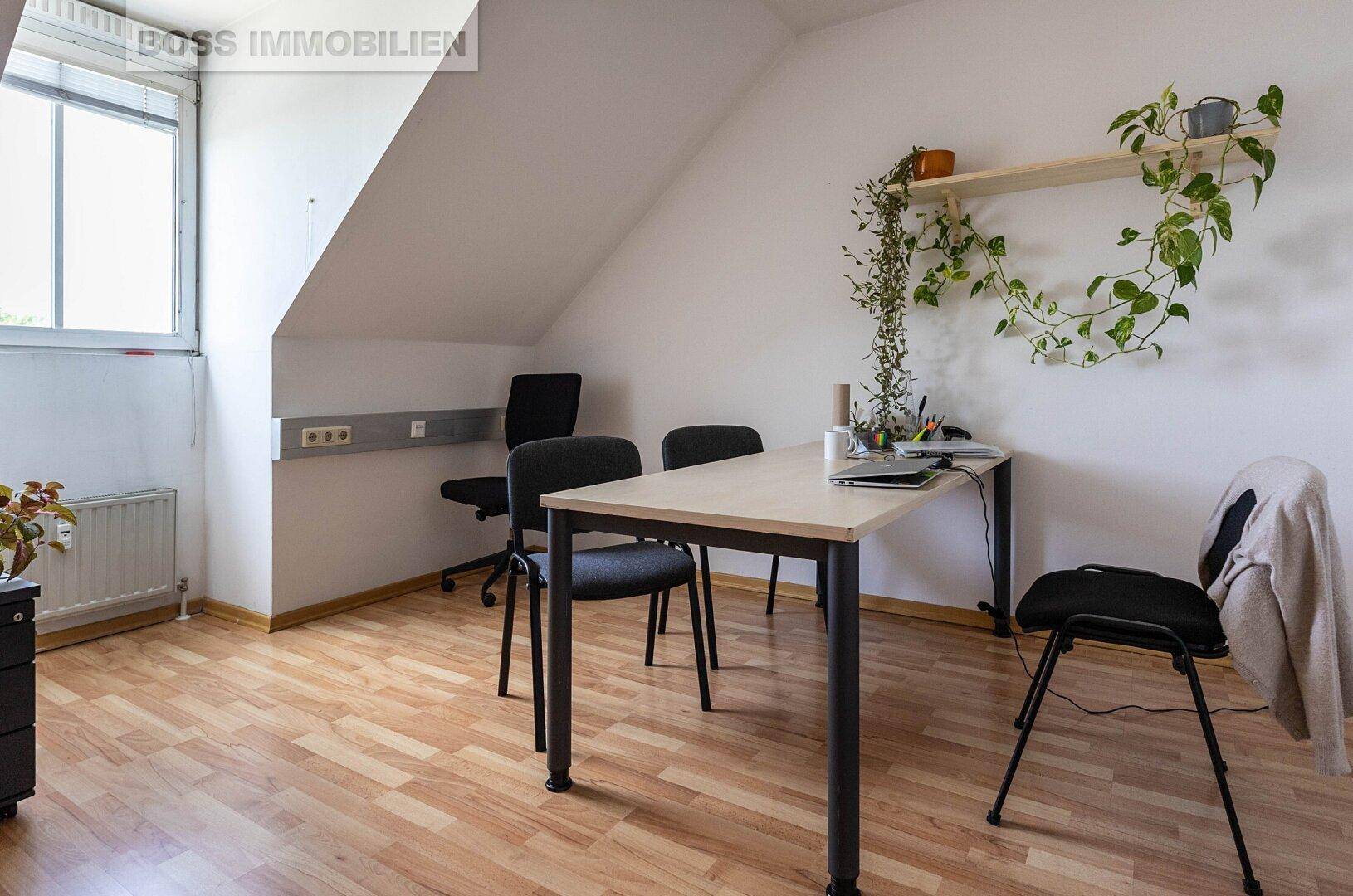 Kleines Büro mit Schreibtisch, Stühlen, einem Fenster und einer Dachschräge, ausgestattet mit Holzfußboden.