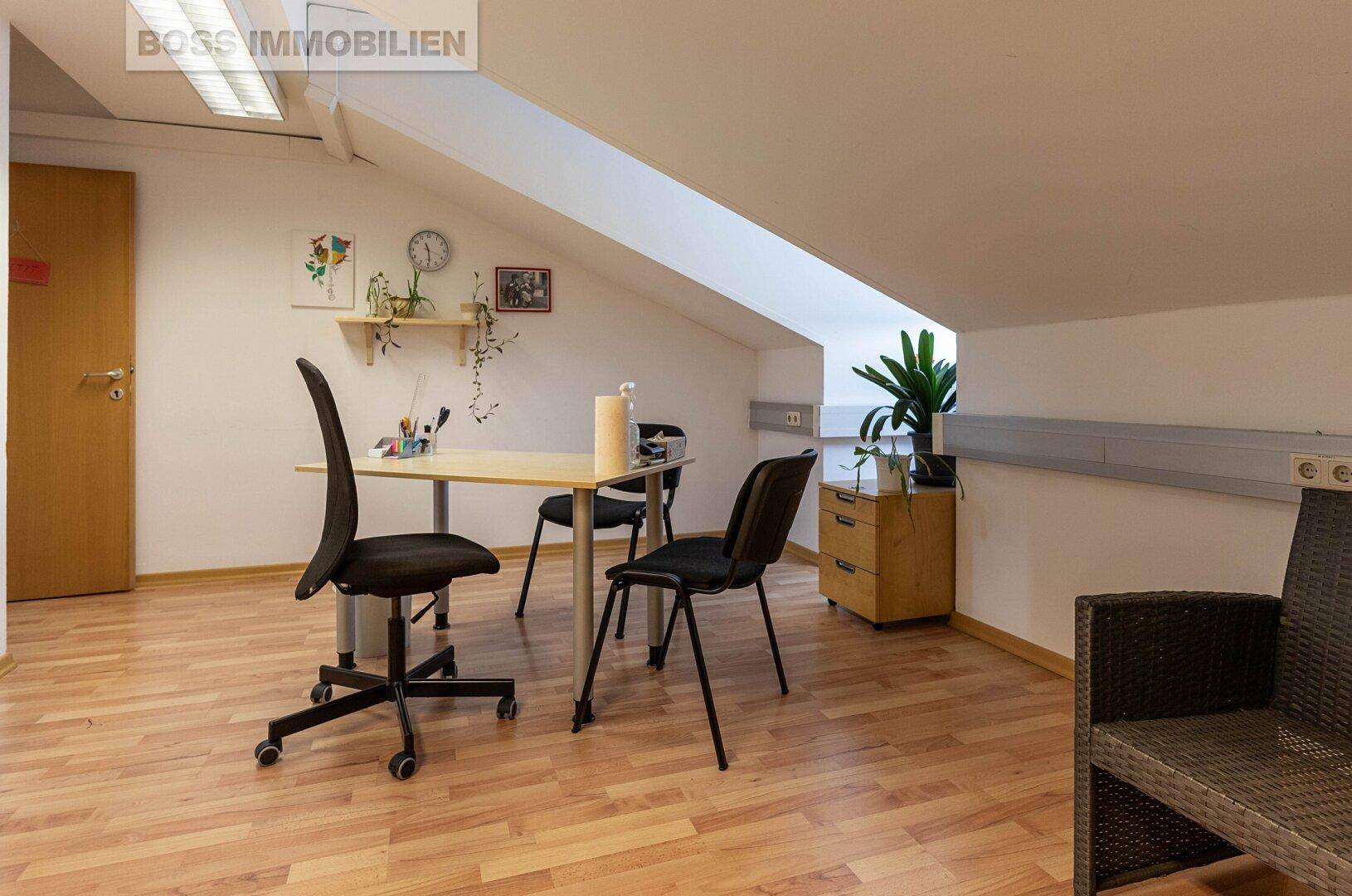 Büro im Dachgeschoss mit Schreibtisch, Bürostühlen und einer markanten Dachschräge, ausgestattet mit Holzfußboden.
