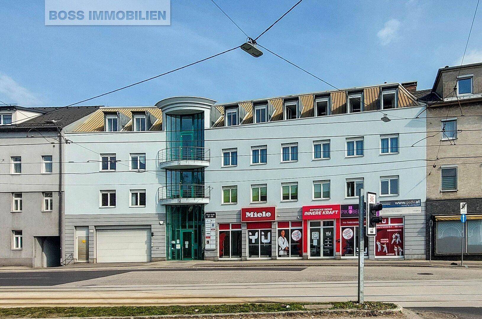 Fassade eines modernen Geschäftsgebäudes mit Ladenlokalen im Erdgeschoss und Büros darüber, an einer Straße gelegen.