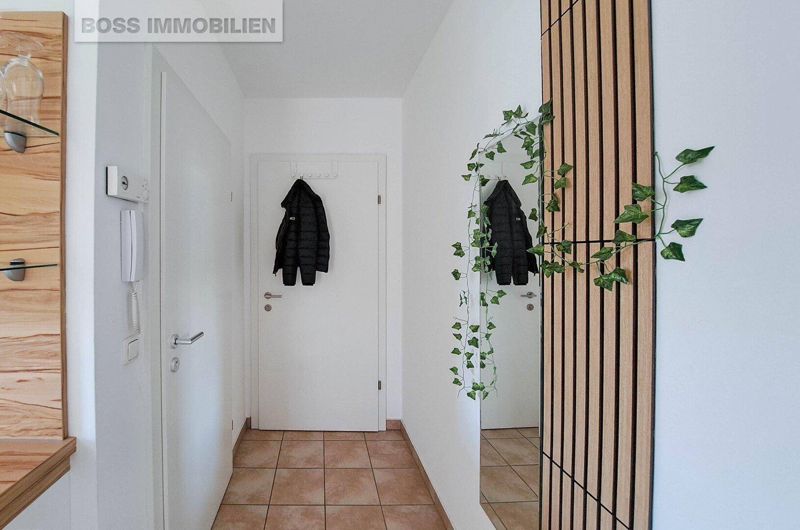 Heller Eingangsbereich mit Fliesenboden, großem Spiegel und Garderobe für Jacken.