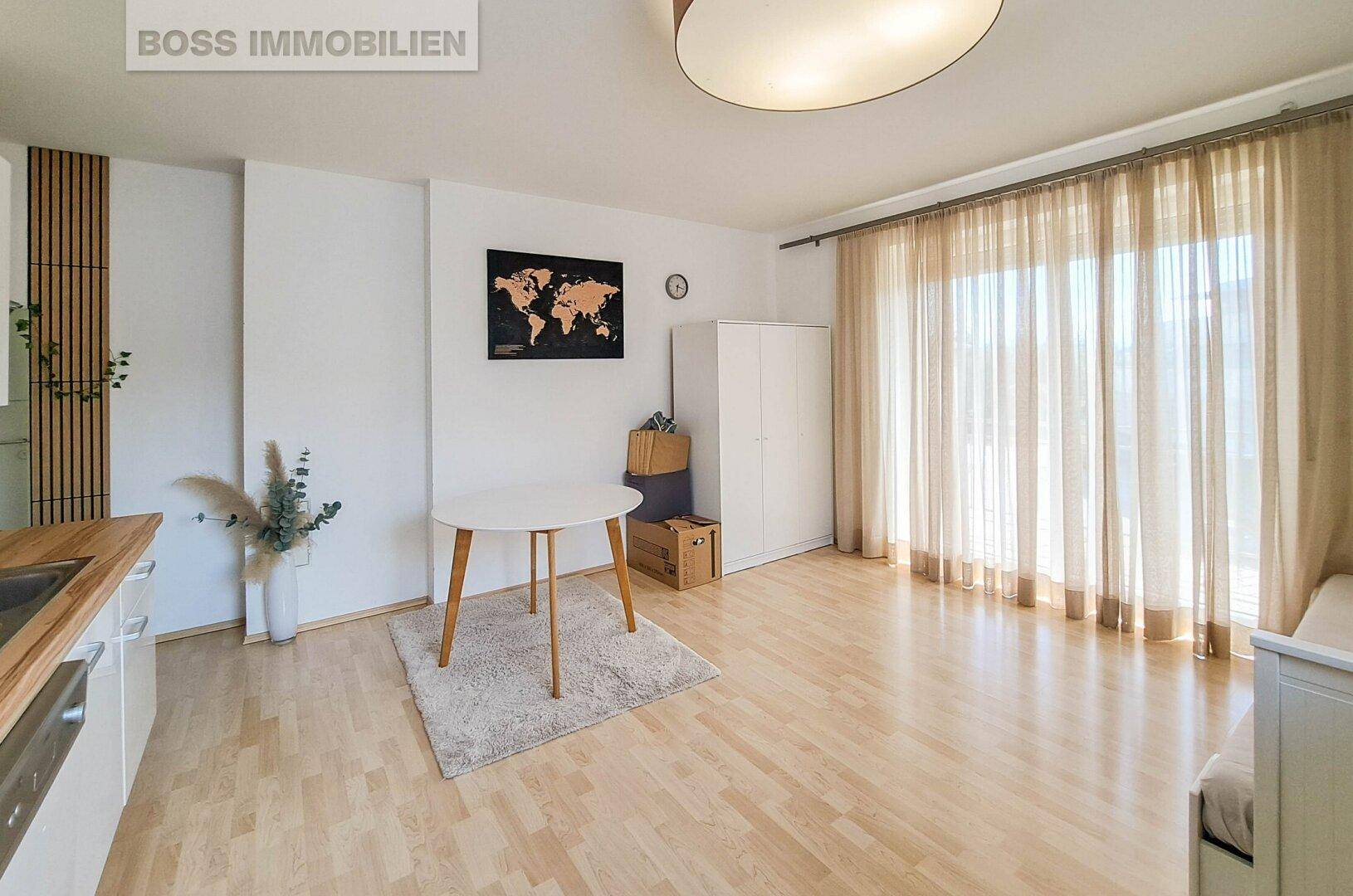Lichtdurchfluteter Wohnbereich mit Esstisch, Kleiderschrank und großen Fenstern mit Vorhängen.