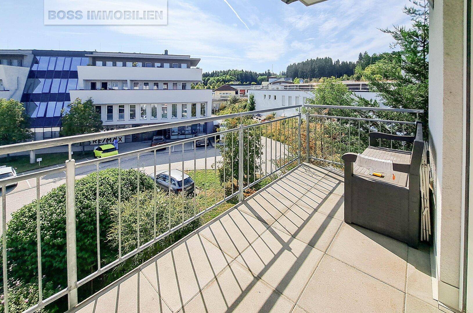 Balkon mit Metallgeländer und Sitzbank bietet Blick auf die umliegenden Gebäude und Grünflächen.