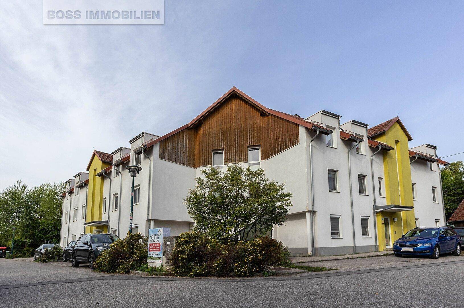 Mehrfamilienhaus mit weißer Fassade, gelben Akzenten und Satteldach in einer Wohngegend.