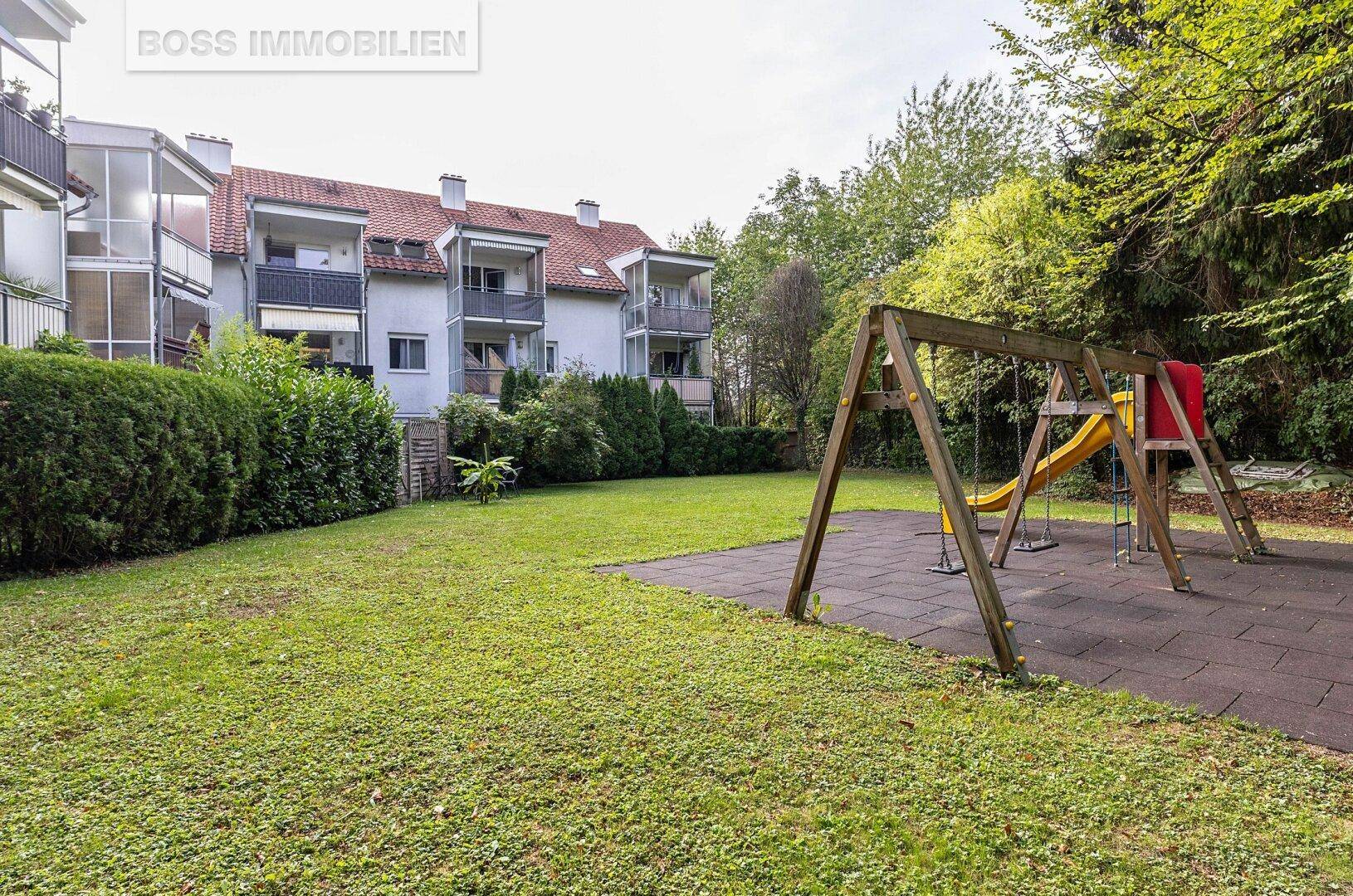 Großer Gemeinschaftsgarten mit Spielplatz und Rutsche, umgeben von Bäumen und Hecken.