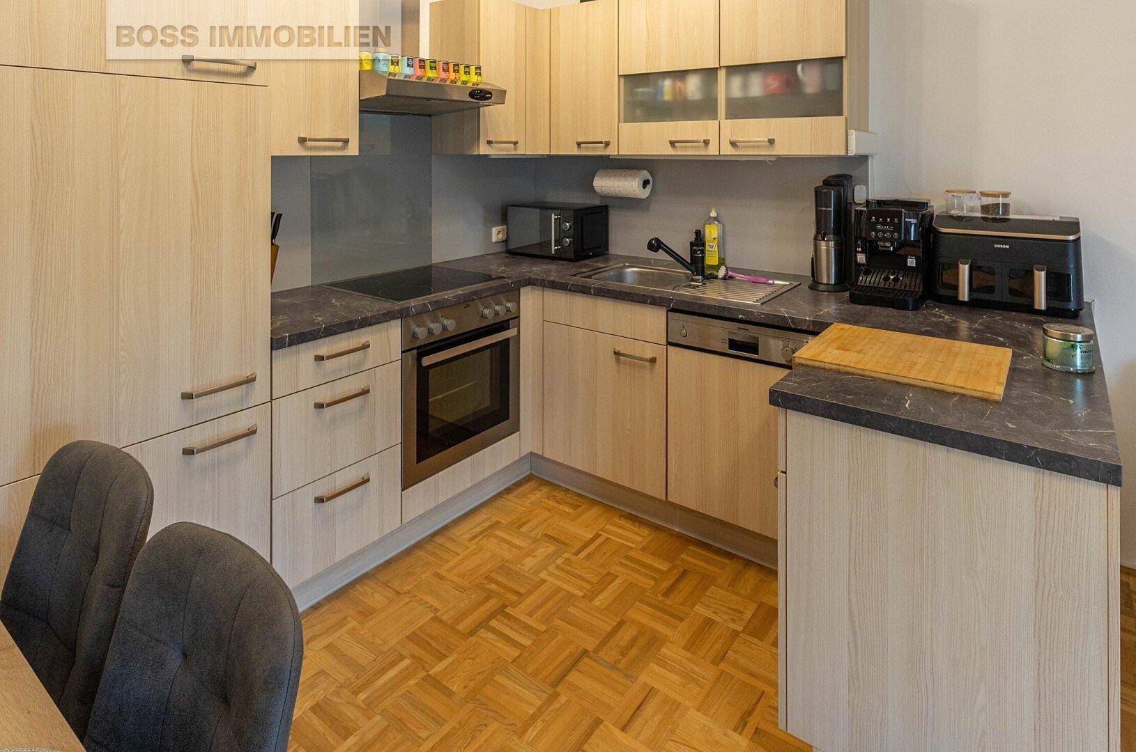 Funktionale Einbauküche mit hellen Holzfronten, dunkler Arbeitsplatte und modernen Geräten.