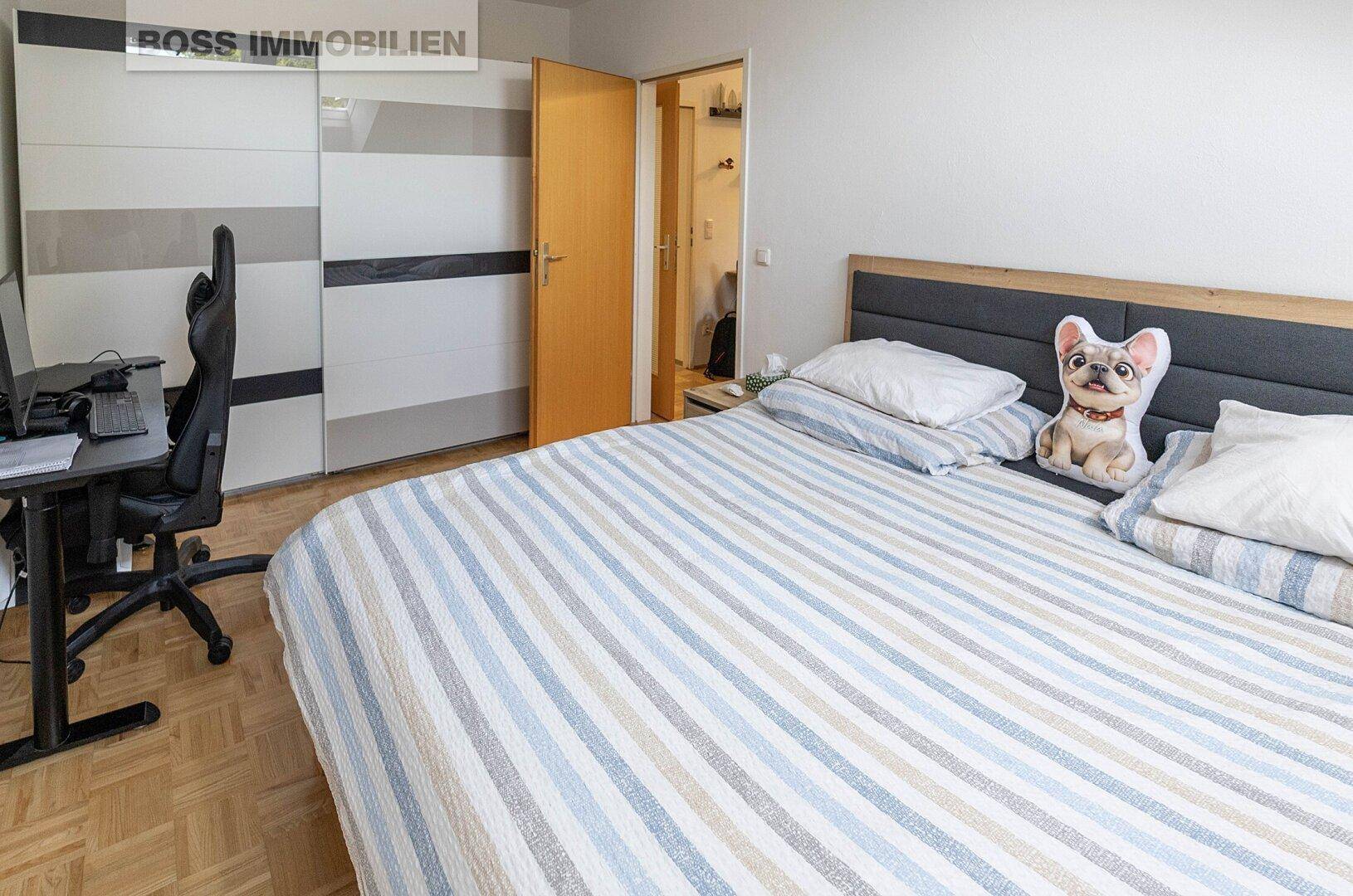 Schlafzimmer mit Doppelbett, Schreibtisch und großem Kleiderschrank auf Parkettboden.
