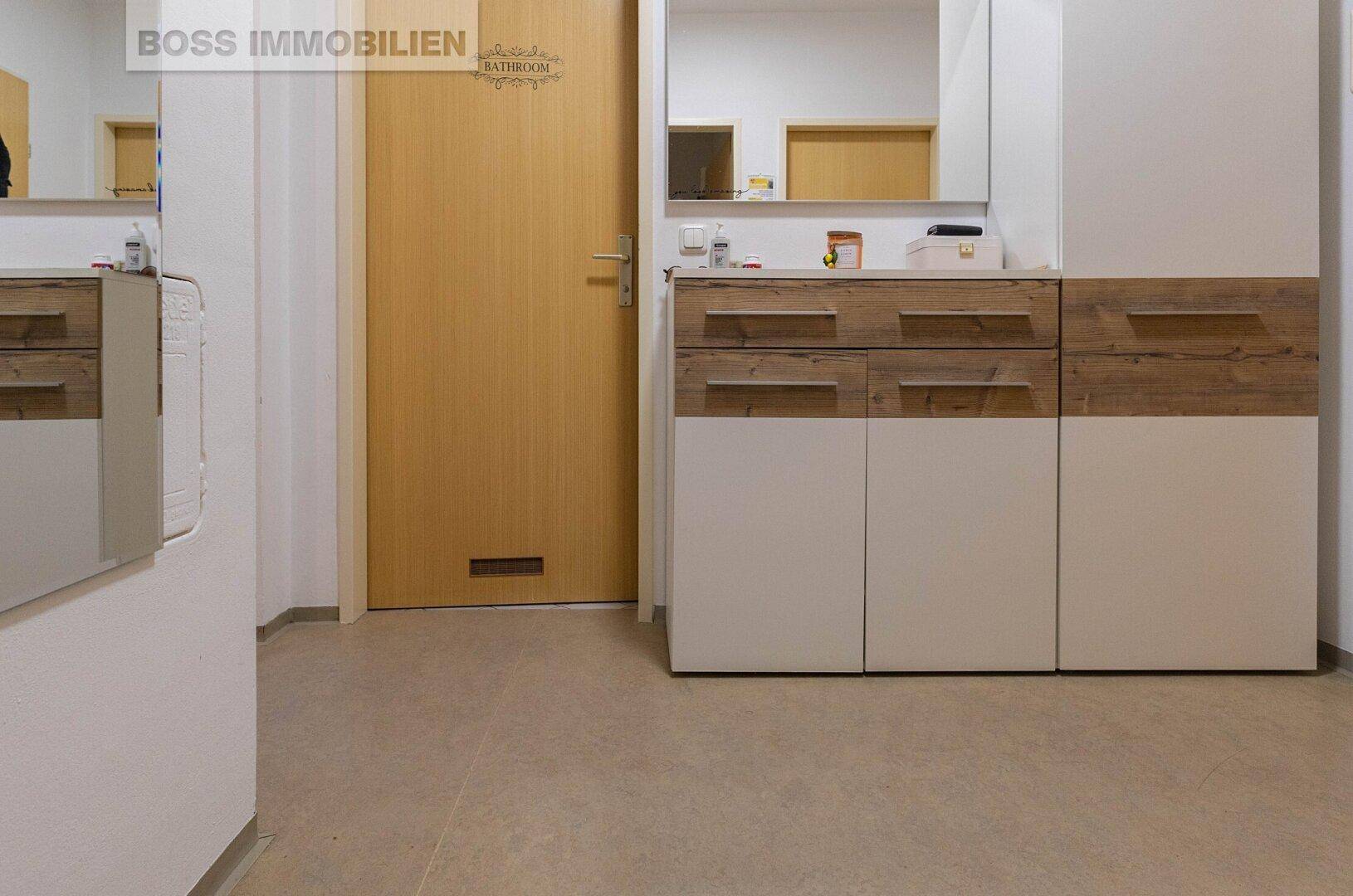 Heller Eingangsbereich mit Garderobe, Spiegel und Holz-Akzenten auf hellem Boden.