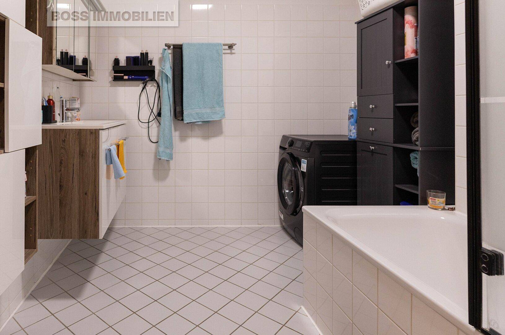 Modern gefliestes Badezimmer mit Badewanne, Waschmaschine und schwebendem Waschtisch.