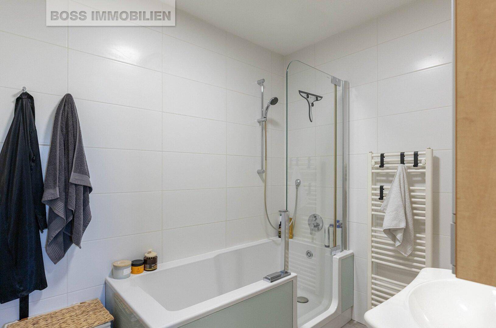 Modernes Badezimmer mit Badewanne, Duschabtrennung und beheiztem Handtuchhalter.
