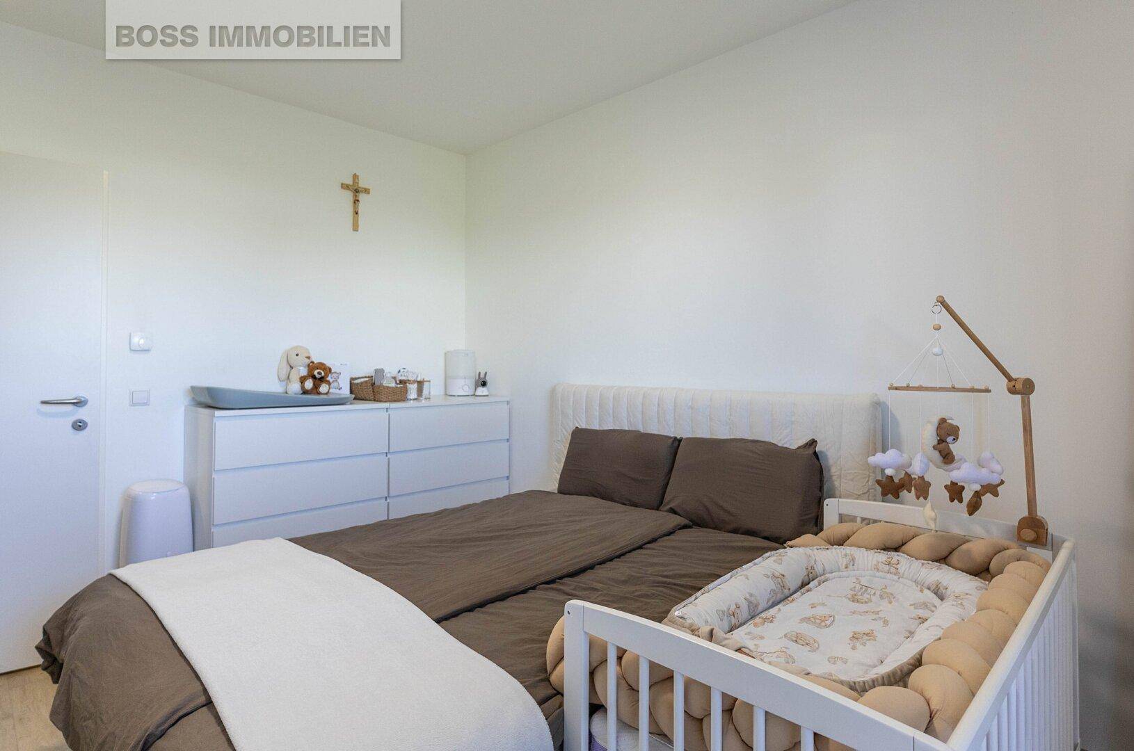 Helles Schlafzimmer mit Doppelbett, Babybett und einer Kommode.