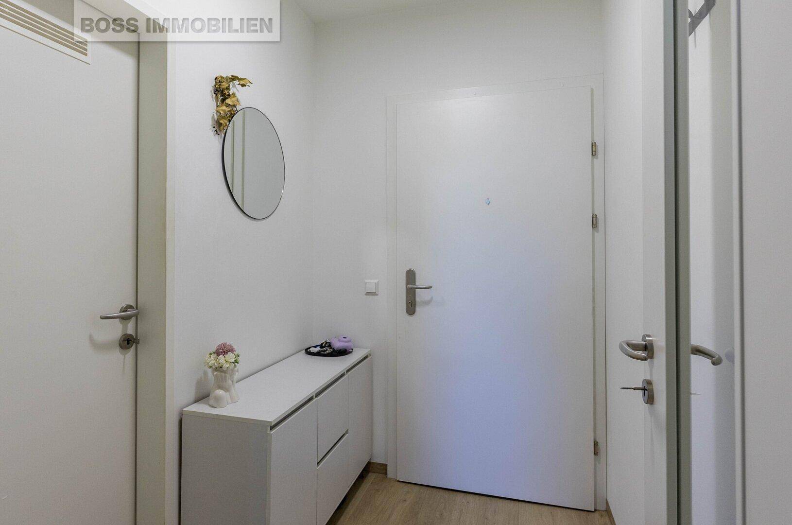 Heller Flur mit Schuhschrank, rundem Spiegel und Zugang zu weiteren Räumen.