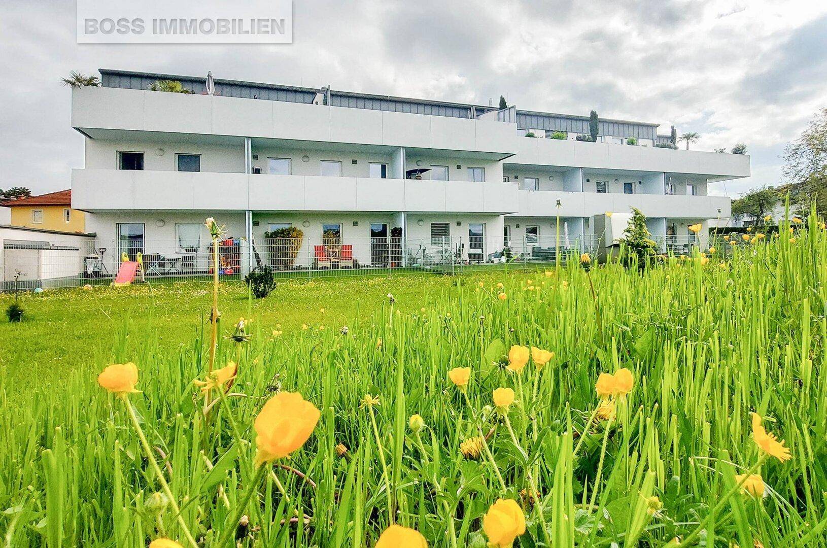 Mehrfamilienhaus mit modernen Balkonen und Terrassen, umgeben von einer grünen Wiese.