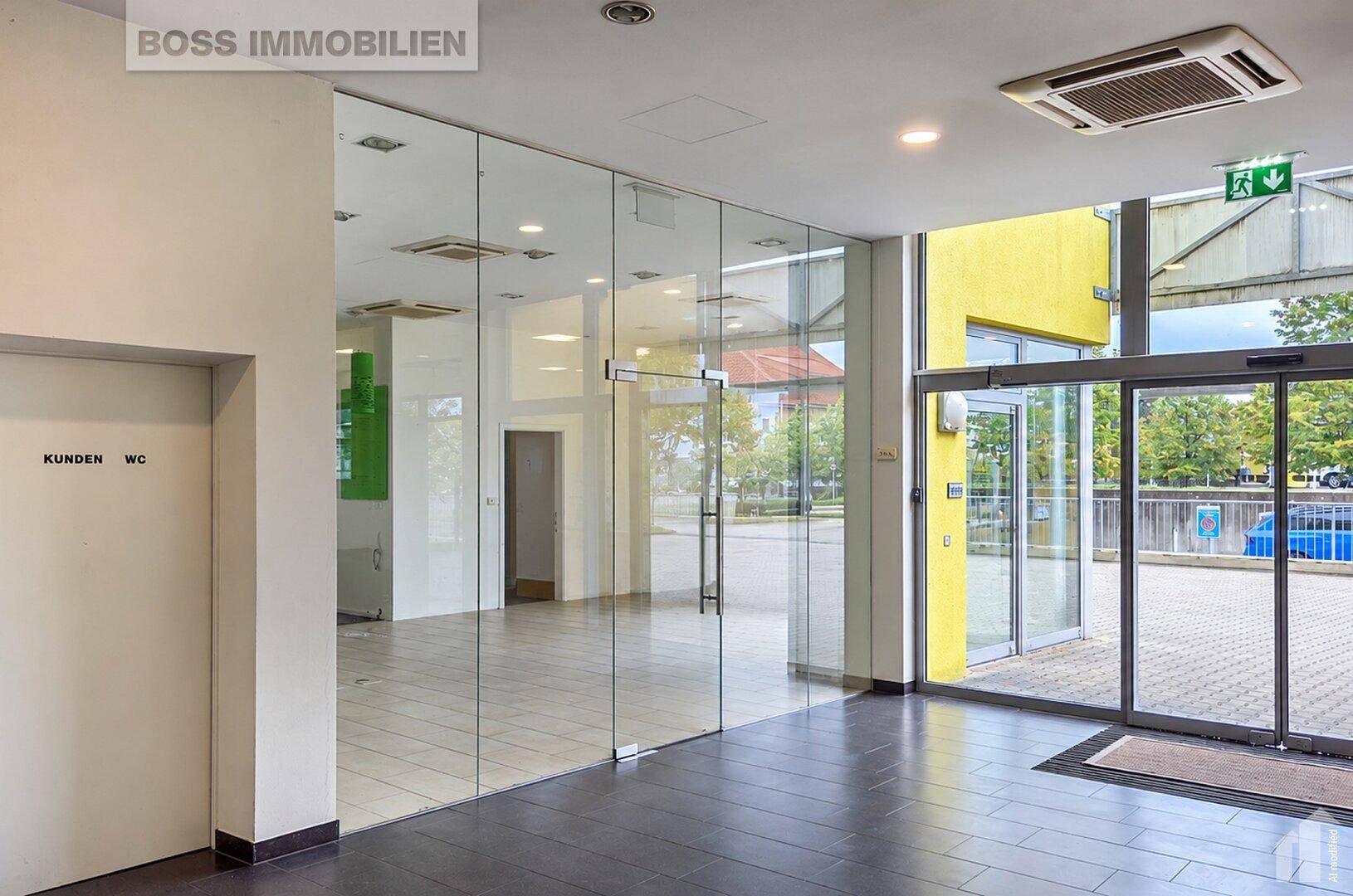 Eingangsbereich eines Gewerberaums mit Glaswänden, dunklem Fliesenboden und Zugang zu den Kunden-WCs.