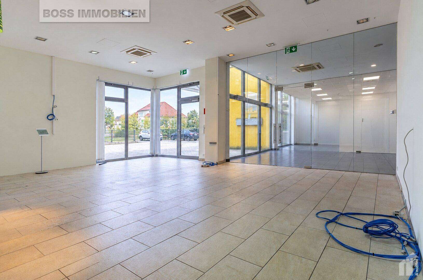 Heller, leerer Gewerberaum mit großen Fensterfronten, Fliesenboden und moderner Deckenbeleuchtung.