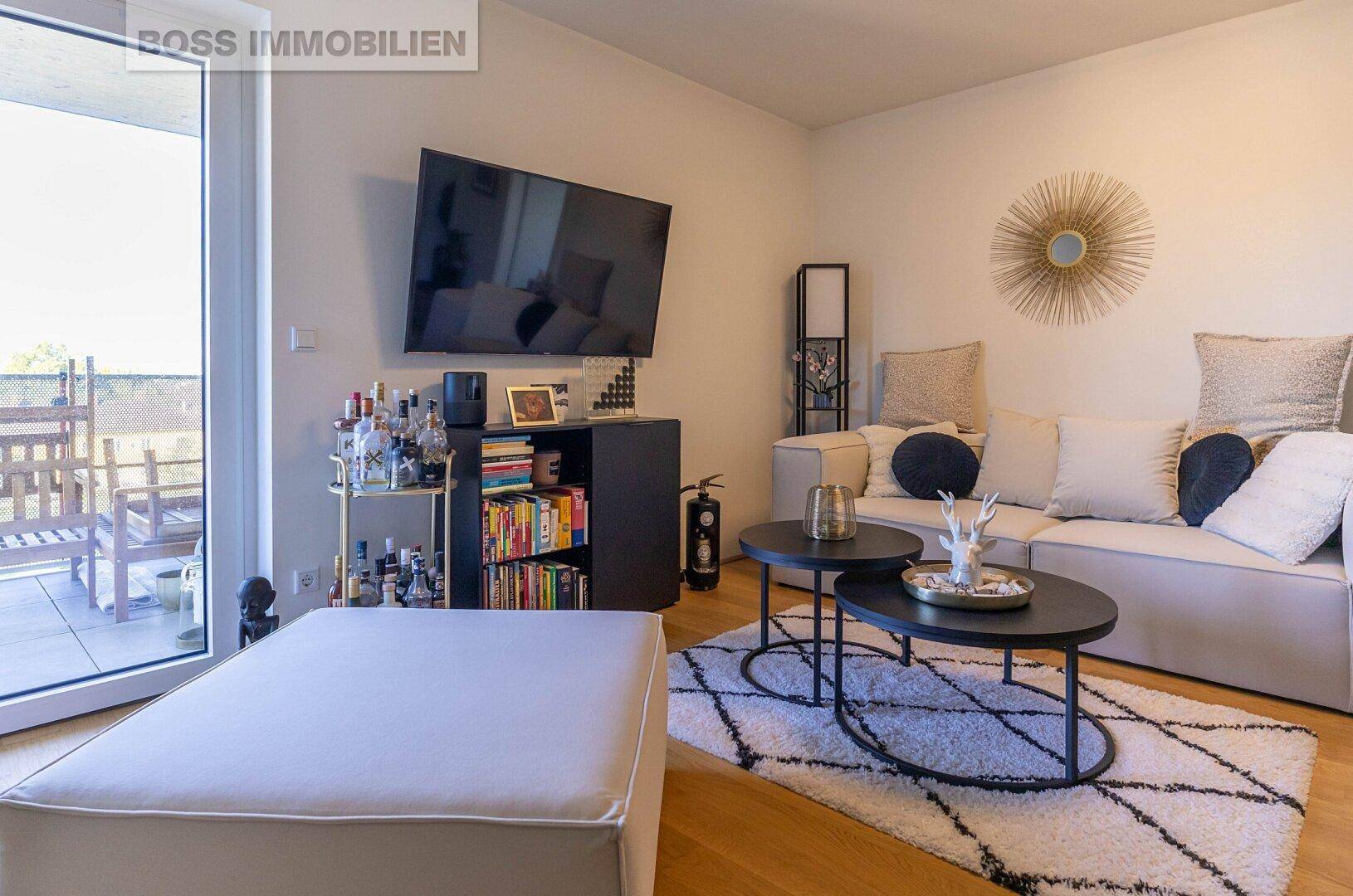 Gemütliches Wohnzimmer mit Sofa, Fernseher und direktem Zugang zu einem möblierten Balkon.