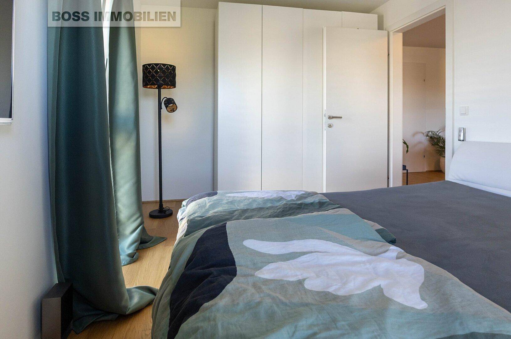 Schlafzimmer mit großem Kleiderschrank, Stehlampe und Zugang zu einem weiteren Raum.