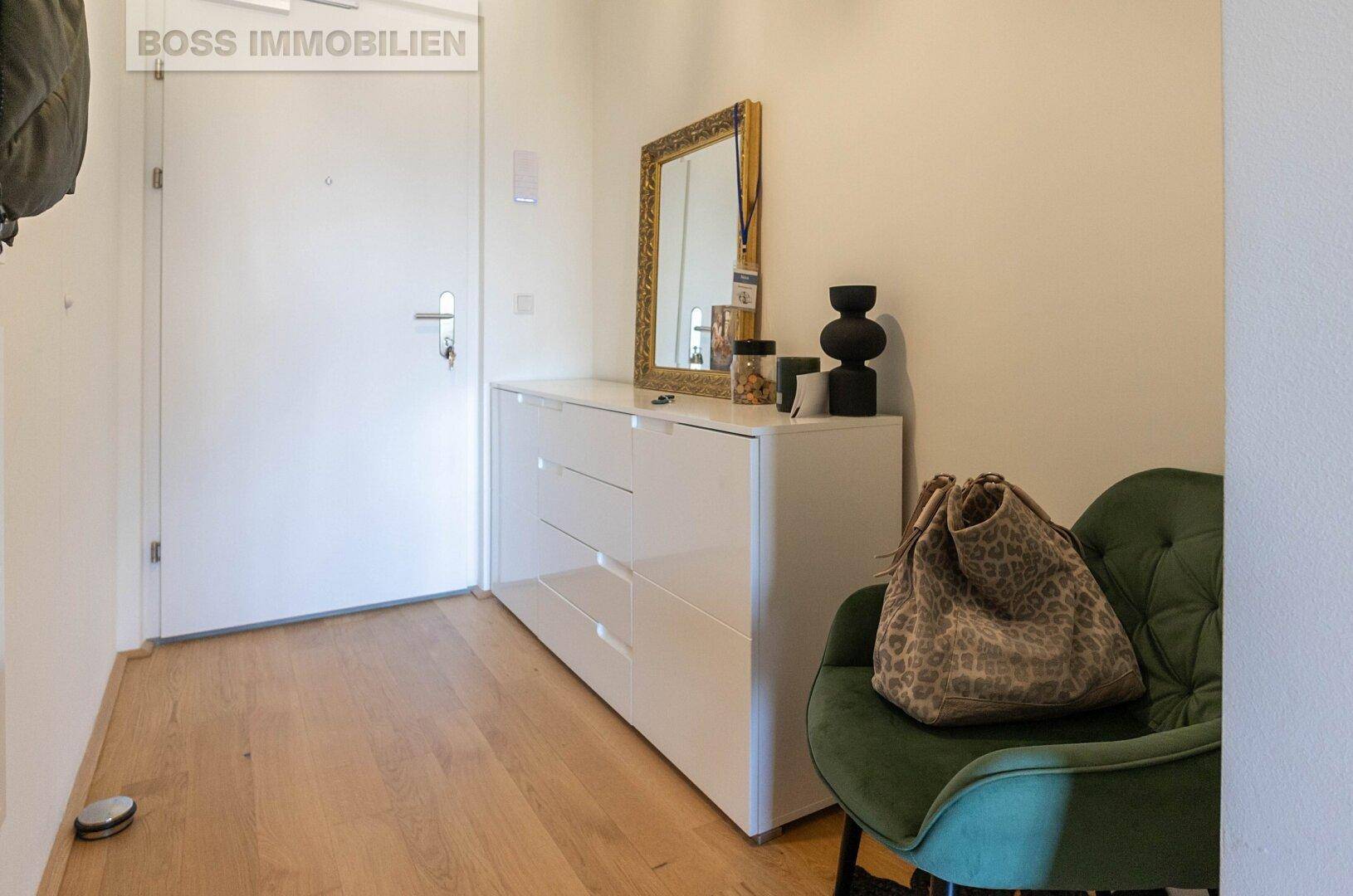 Heller Eingangsbereich mit Kommode, Spiegel und einem bequemen Sessel.