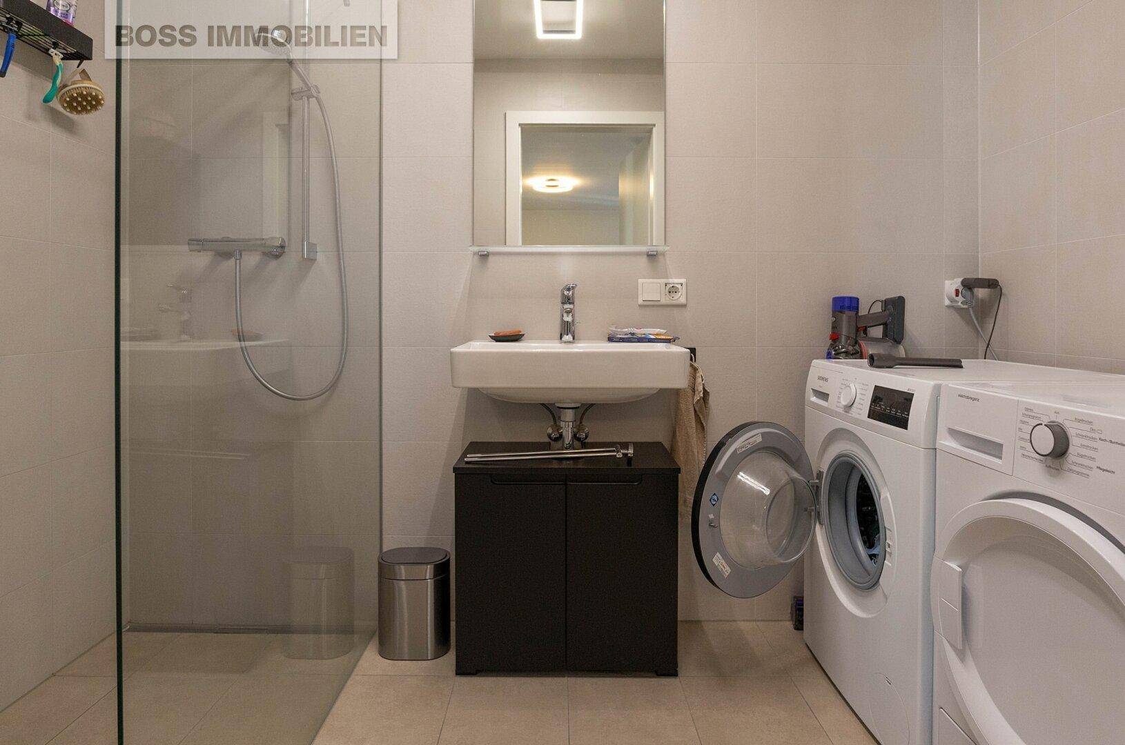 Modernes Badezimmer mit ebenerdiger Dusche, Waschbecken und Waschmaschine.