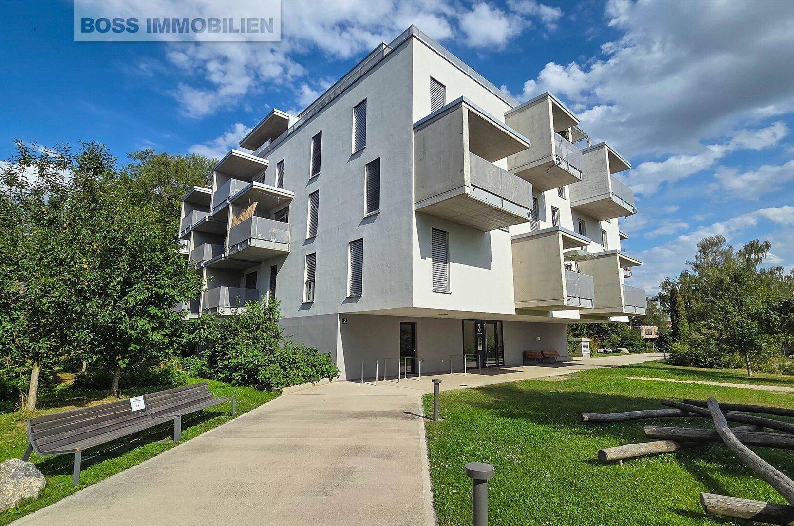 Modernes Mehrfamilienhaus mit mehreren Balkonen und grüner Umgebung.