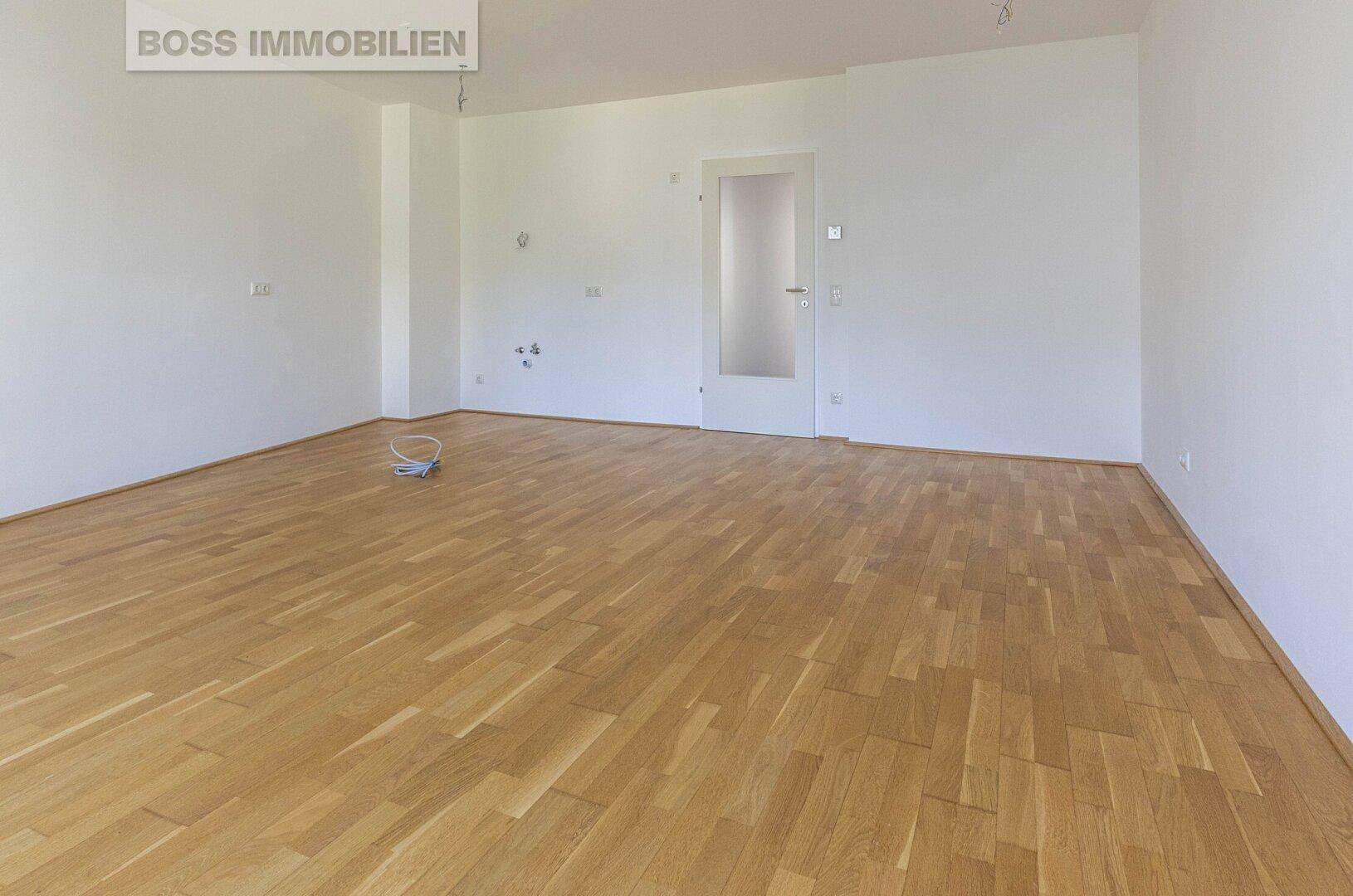 Leeres Wohnzimmer mit hellem Parkettboden und weißen Wänden, bereit zum Einzug.