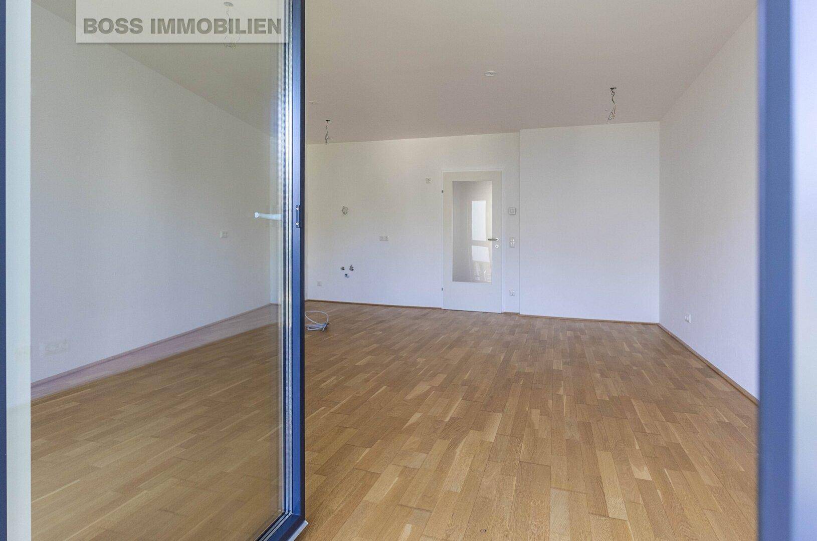 Geräumiges, leeres Wohnzimmer mit Parkettboden und Blick auf eine Innentür.