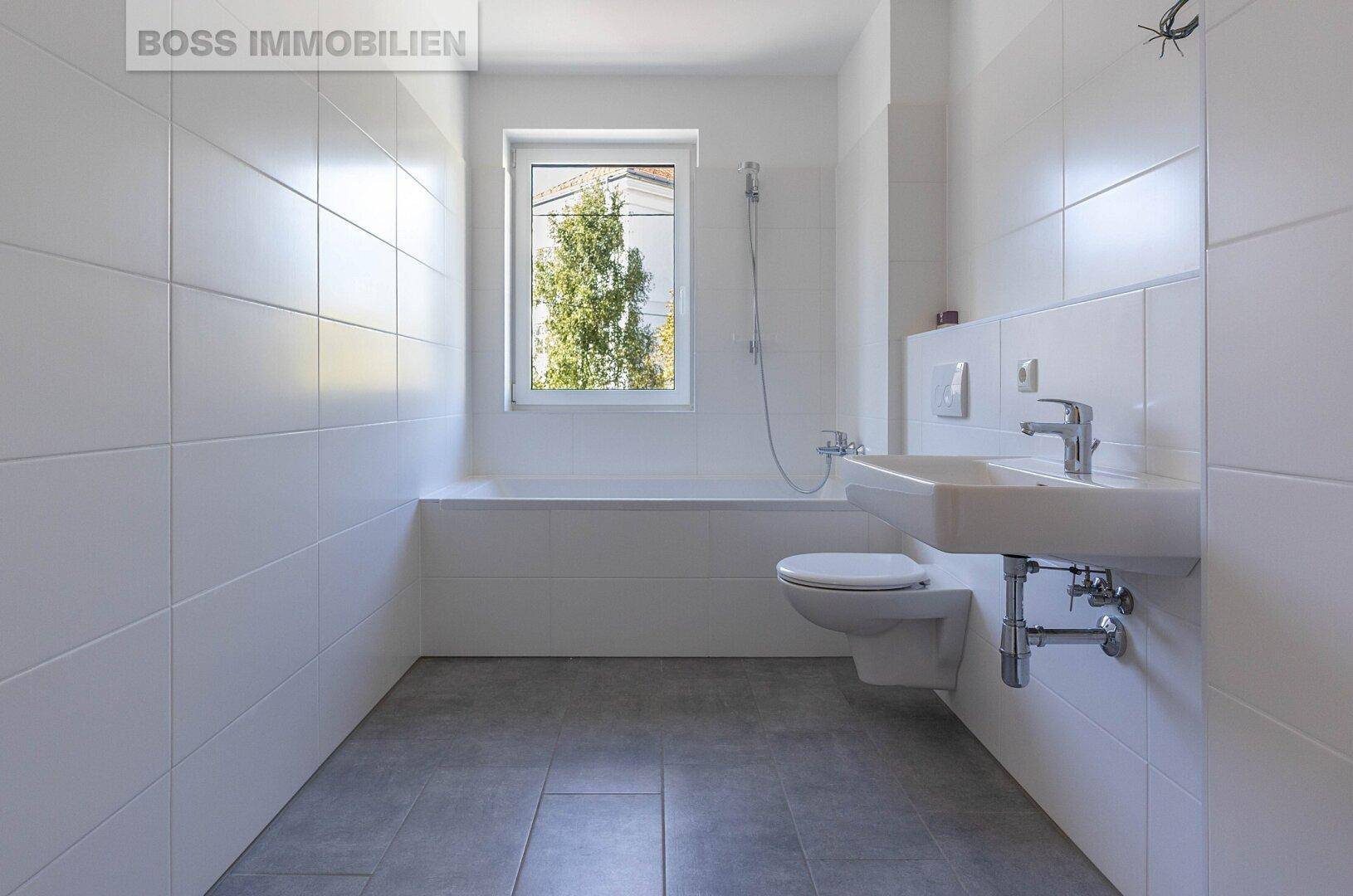 Modernes Badezimmer mit weißen Fliesen, Badewanne und Fenster für Tageslicht.