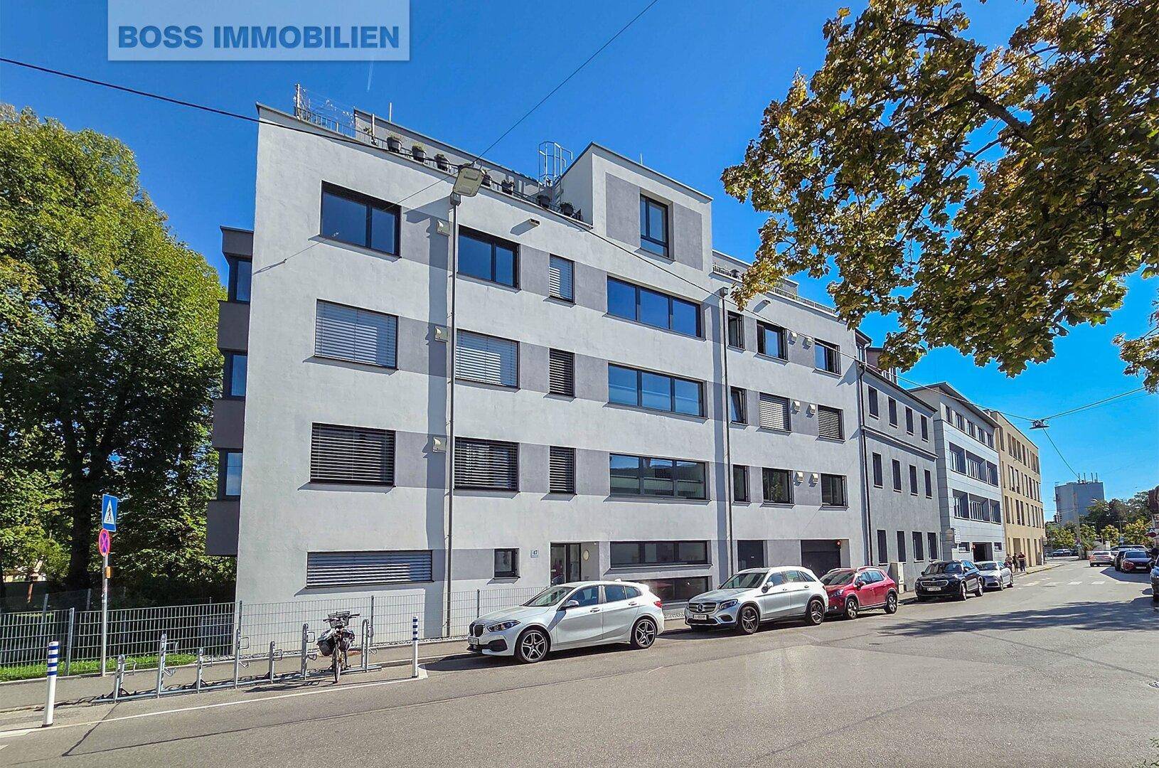 Moderne Wohnanlage an einer städtischen Straße mit parkenden Autos und Bäumen.