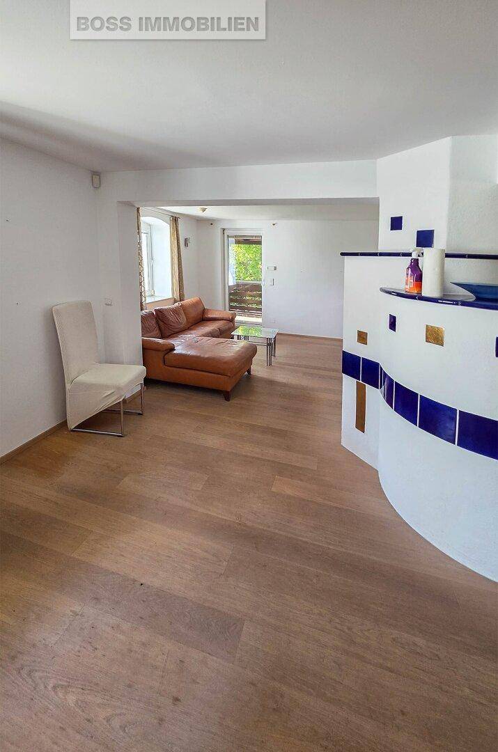 Helles Wohnzimmer mit Holzboden, Ledersofa und einem dekorativen Kachelofen.