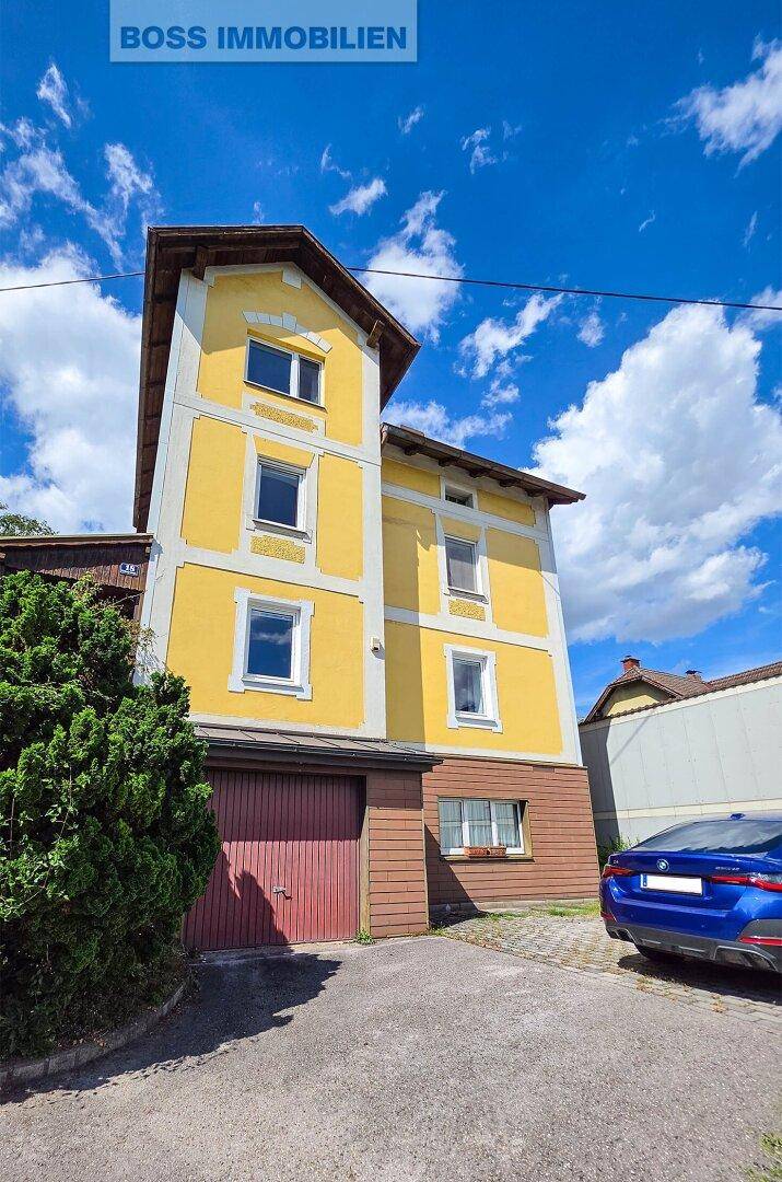 Ansicht des gelben Mehrfamilienhauses mit Garagentor und einem geparkten blauen Auto davor.