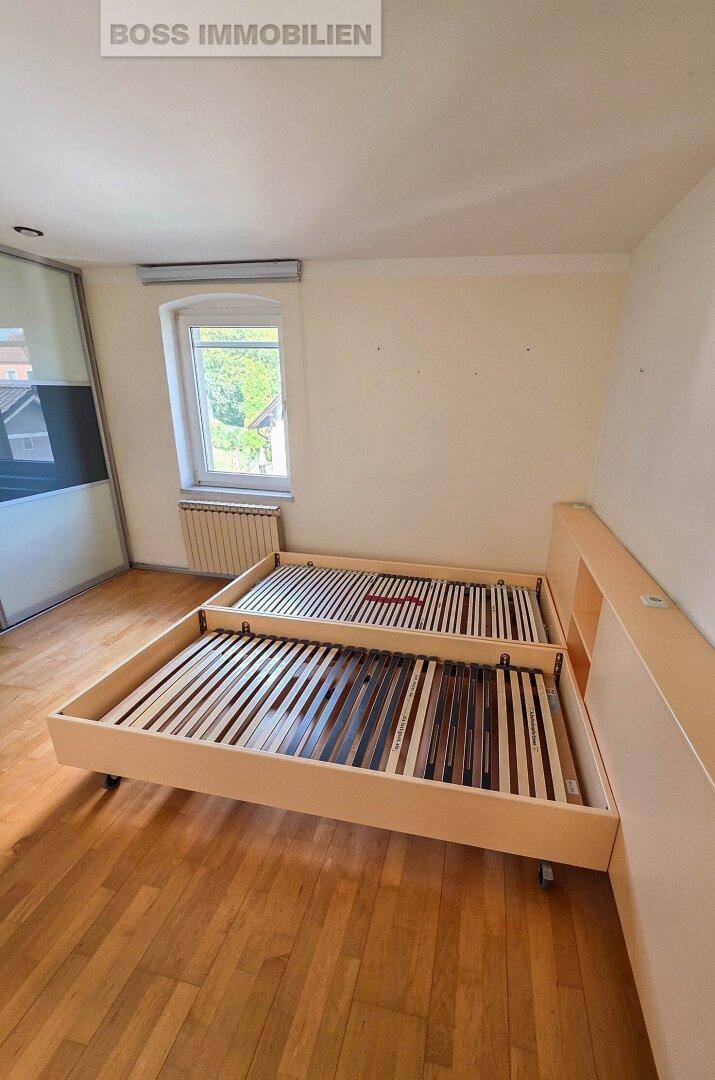 Schlafzimmer mit Holzboden, Fenster und zwei Bettrahmen, die auf den Einbau warten.