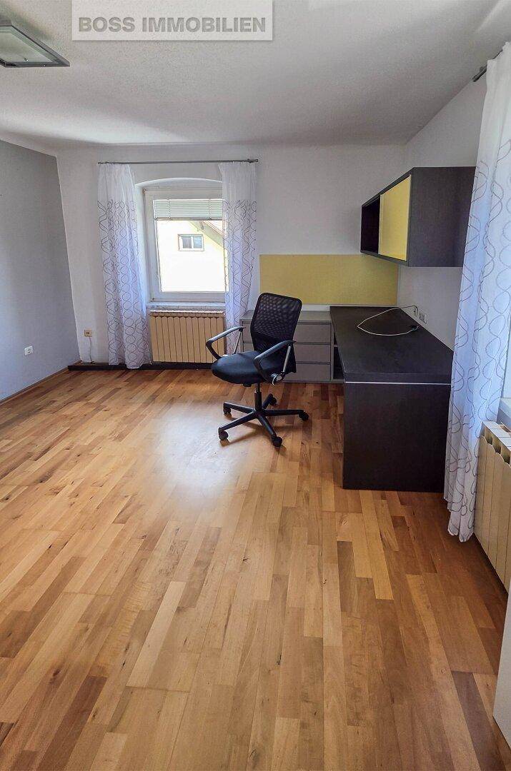 Helles Arbeitszimmer mit Holzboden, Schreibtisch und einem Fenster mit Blick ins Grüne.