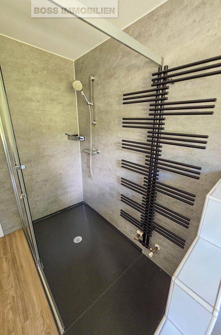 Geräumige begehbare Dusche mit modernen Fliesen und einem schwarzen Handtuchheizkörper.