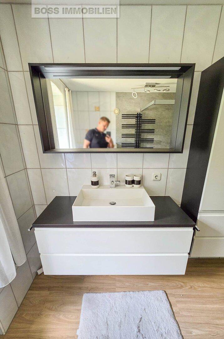 Modernes Badezimmer mit Waschbecken, Spiegel und beheiztem Handtuchhalter an der Wand.