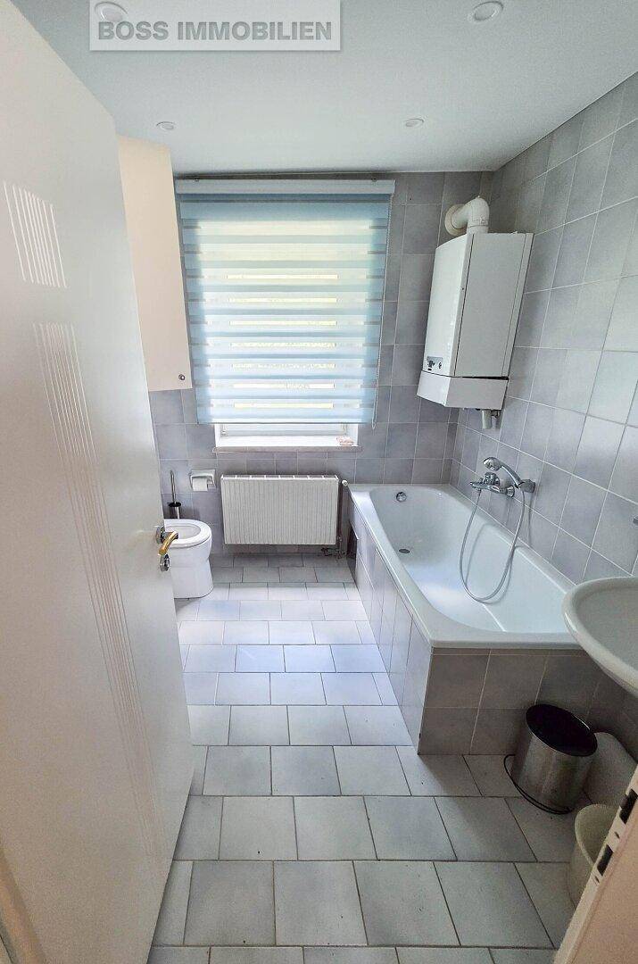 Badezimmer mit Badewanne, WC und Waschbecken, ausgestattet mit hellgrauen Fliesen.