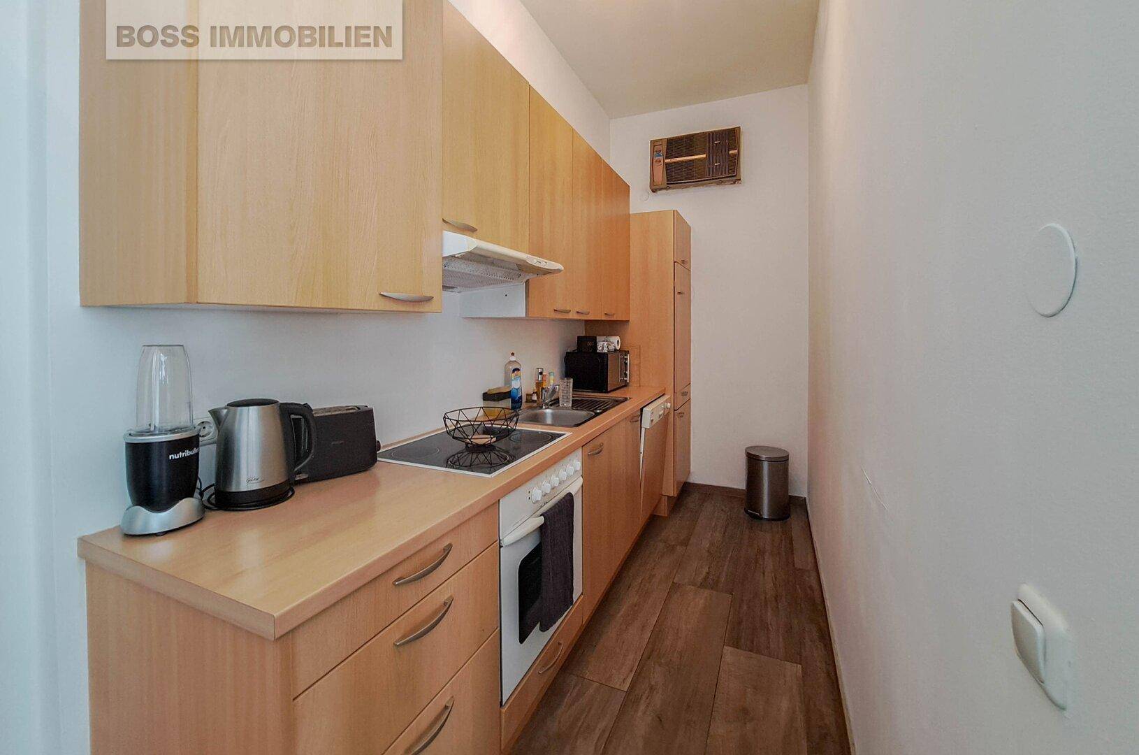 Schmale Küche mit hellen Holzschränken, Einbaugeräten und Holzboden.
