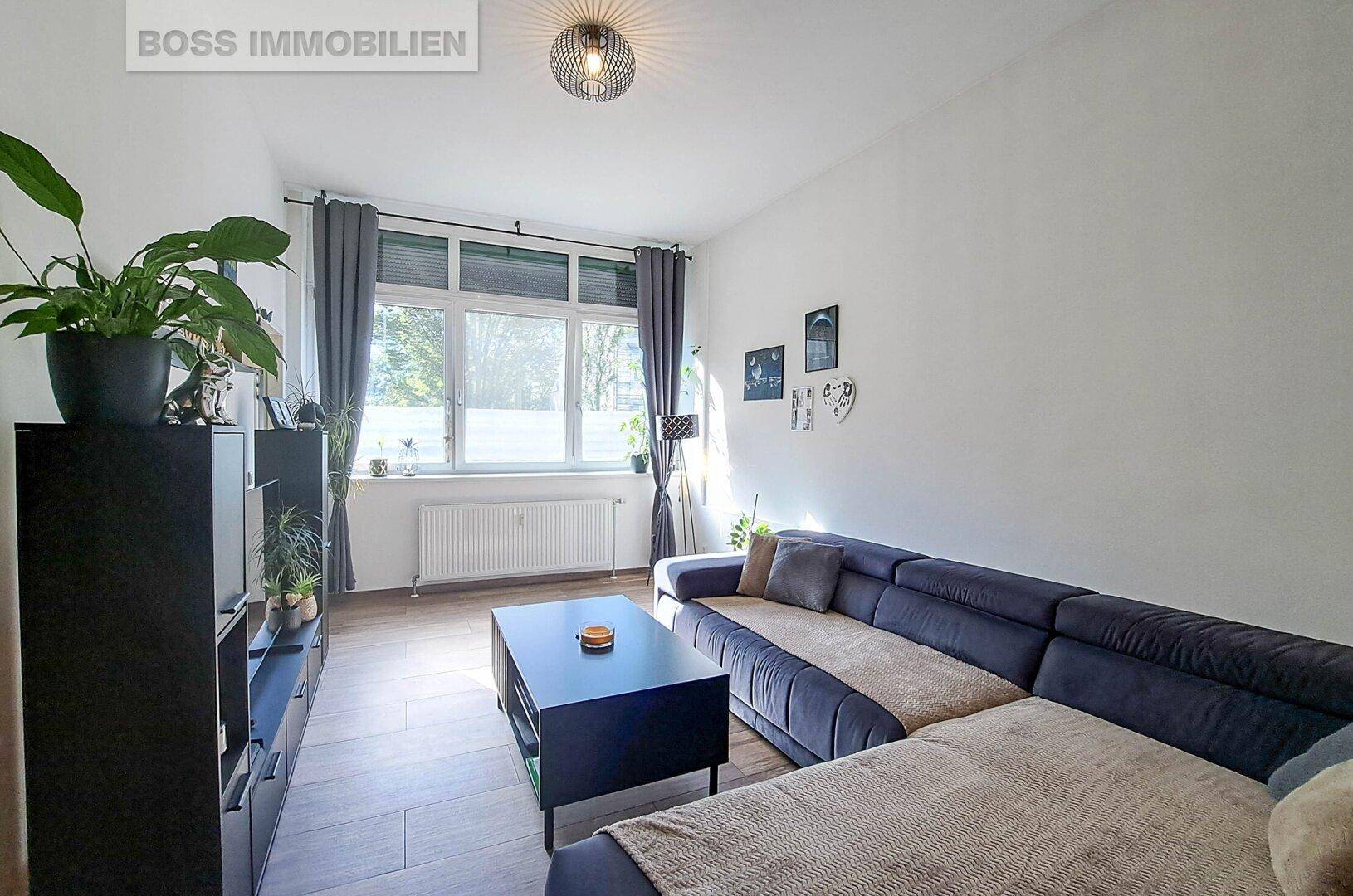 Helles Wohnzimmer mit großem Sofa, Holzboden und Blick ins Grüne.