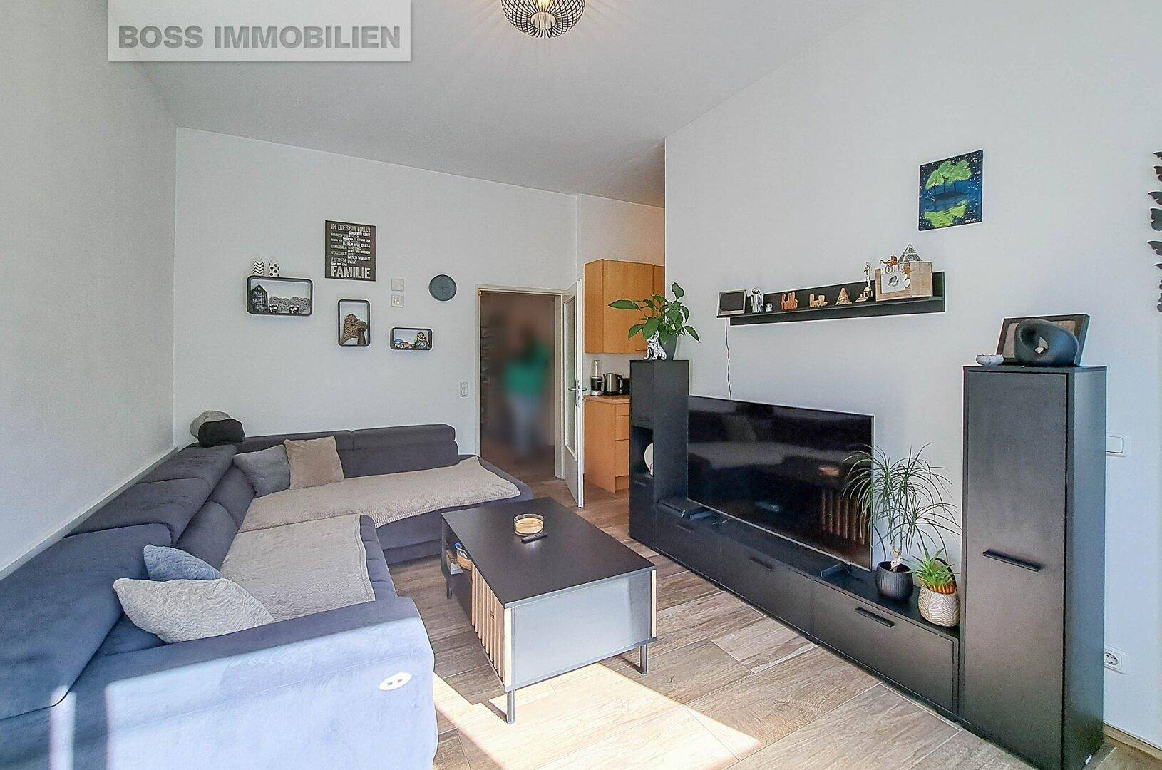 Wohnzimmer mit Sofa, Fernseher und offenem Zugang zu einer kleinen Küche.