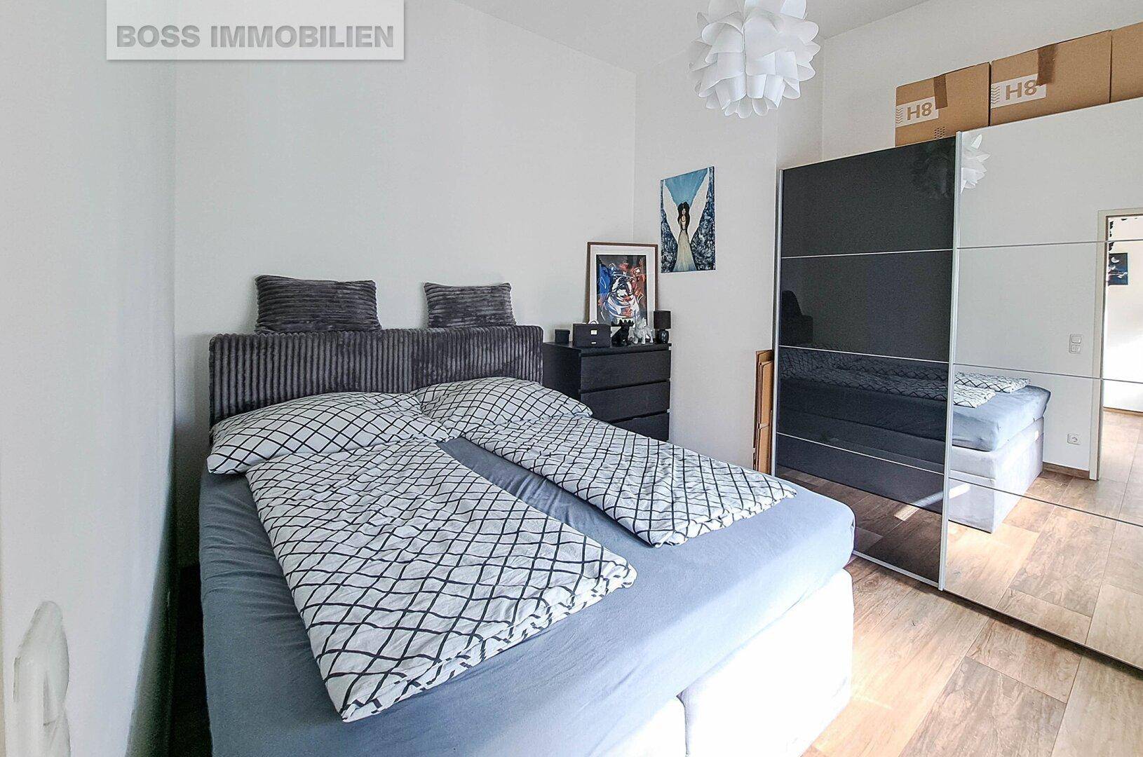 Helles Schlafzimmer mit Doppelbett, Spiegelschrank und modernem Dekor auf Holzboden.