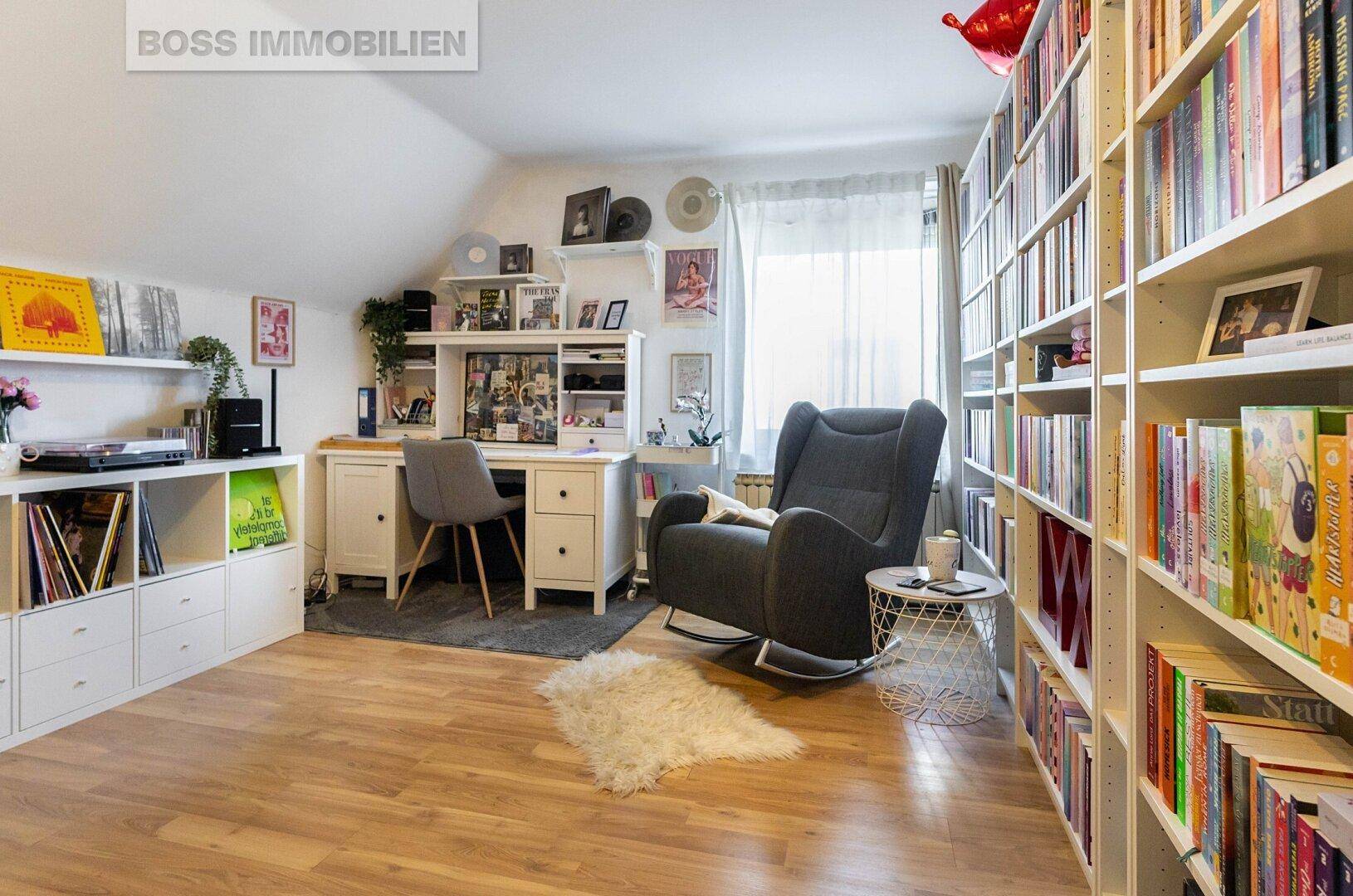 Helles Arbeitszimmer mit umfangreichen Bücherregalen, Schreibtisch und Lesesessel.