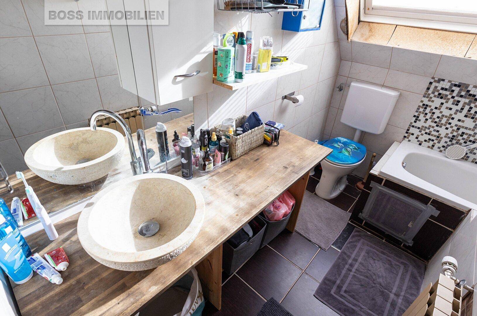 Badezimmer mit zwei Aufsatzwaschbecken, WC und kleiner Badewanne unter Dachschräge.
