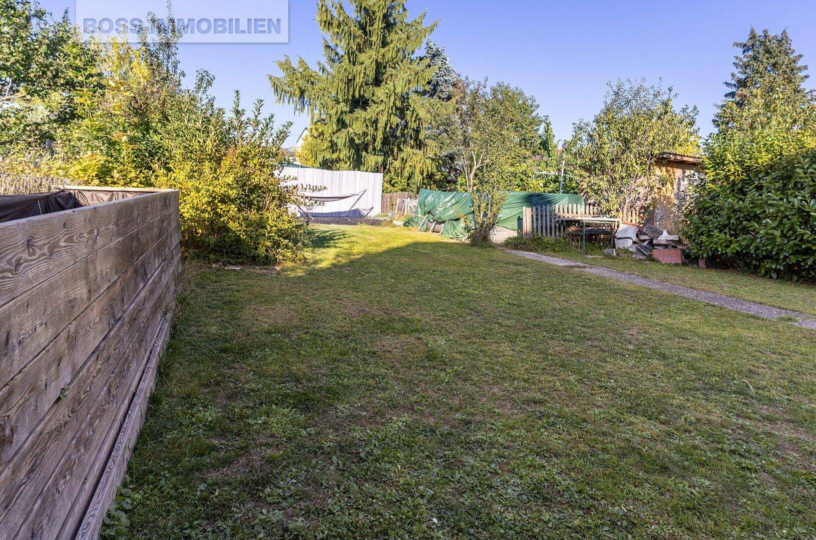 Großer, gepflegter Garten mit Rasenfläche, Bäumen und Holzzaun.