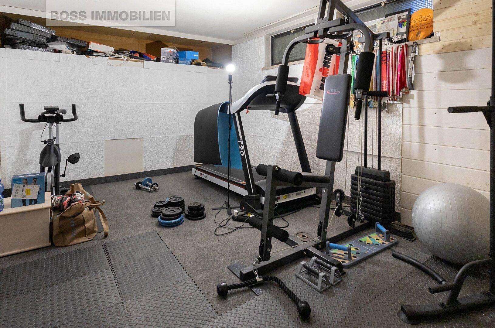Fitnessraum im Untergeschoss mit Laufband, Hanteln und verschiedenen Trainingsgeräten.